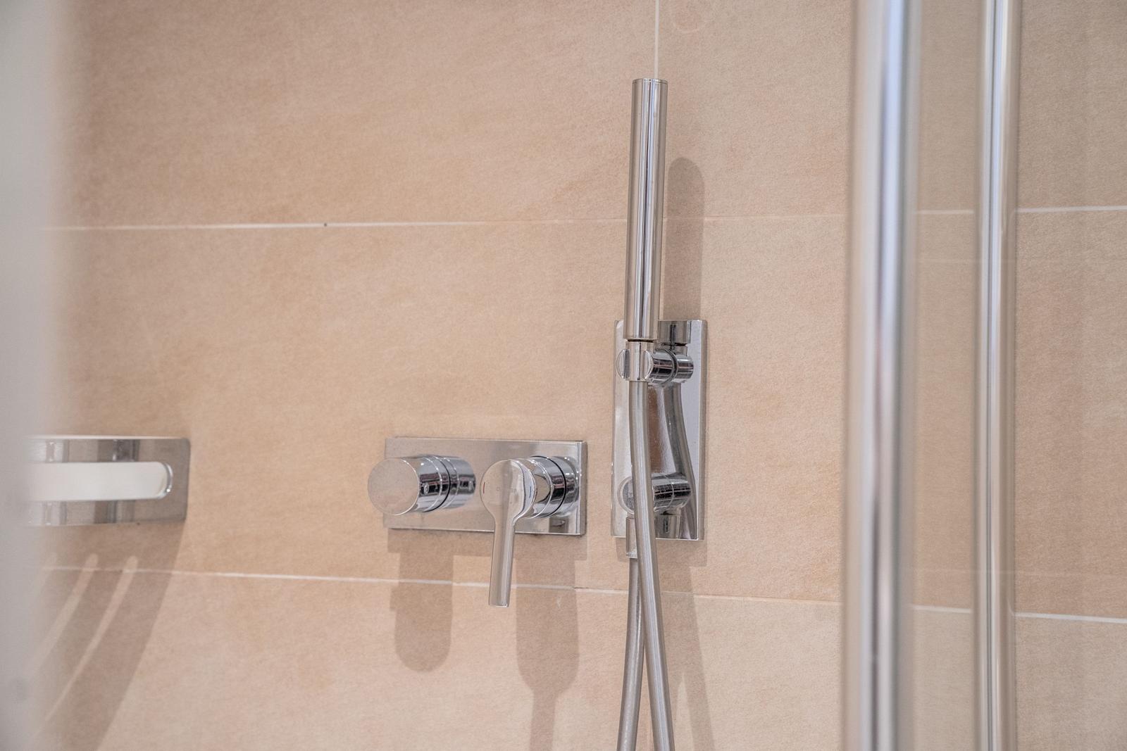 Showerhead with wall-mounted shower and handheld shower on beige tiled wall