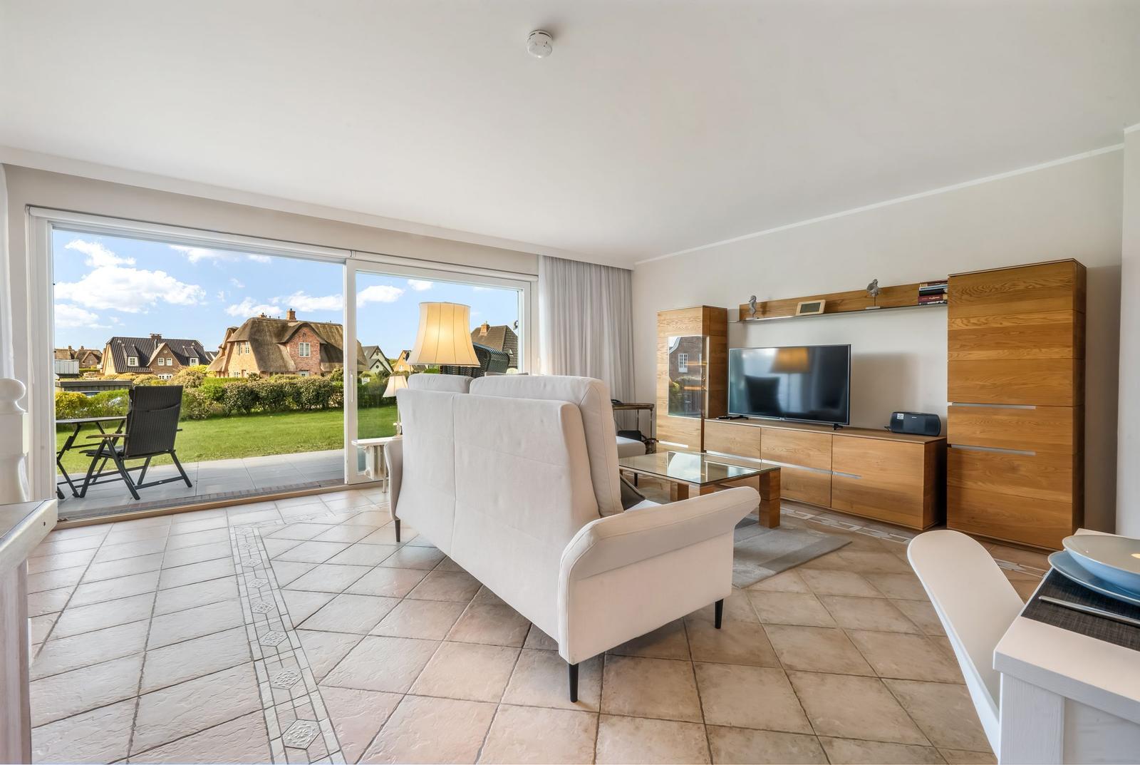 Living room with sofa, TV, and view of garden and houses.