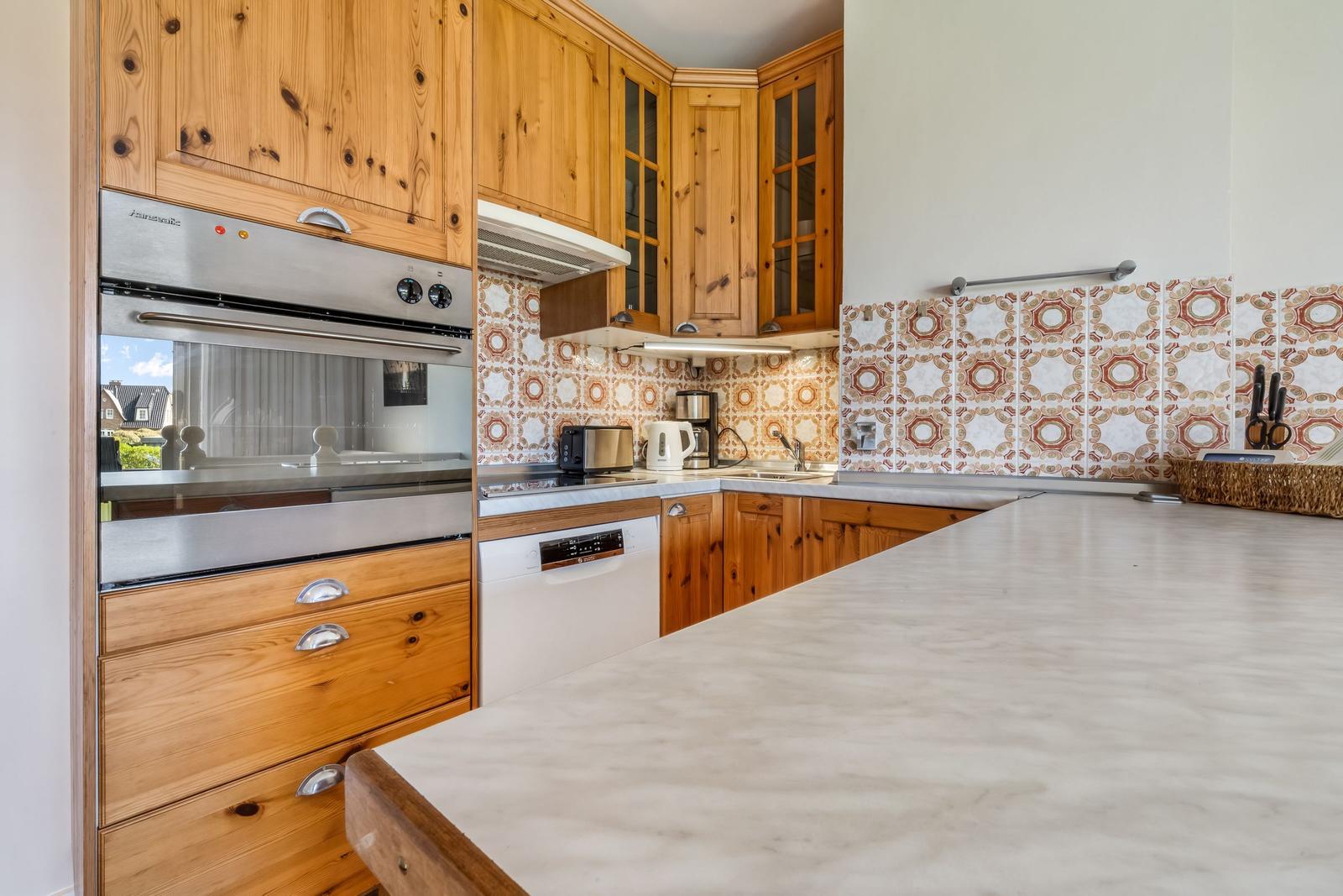 Kitchen with wooden cabinets, marble countertop, and mosaic tiles on the wall.