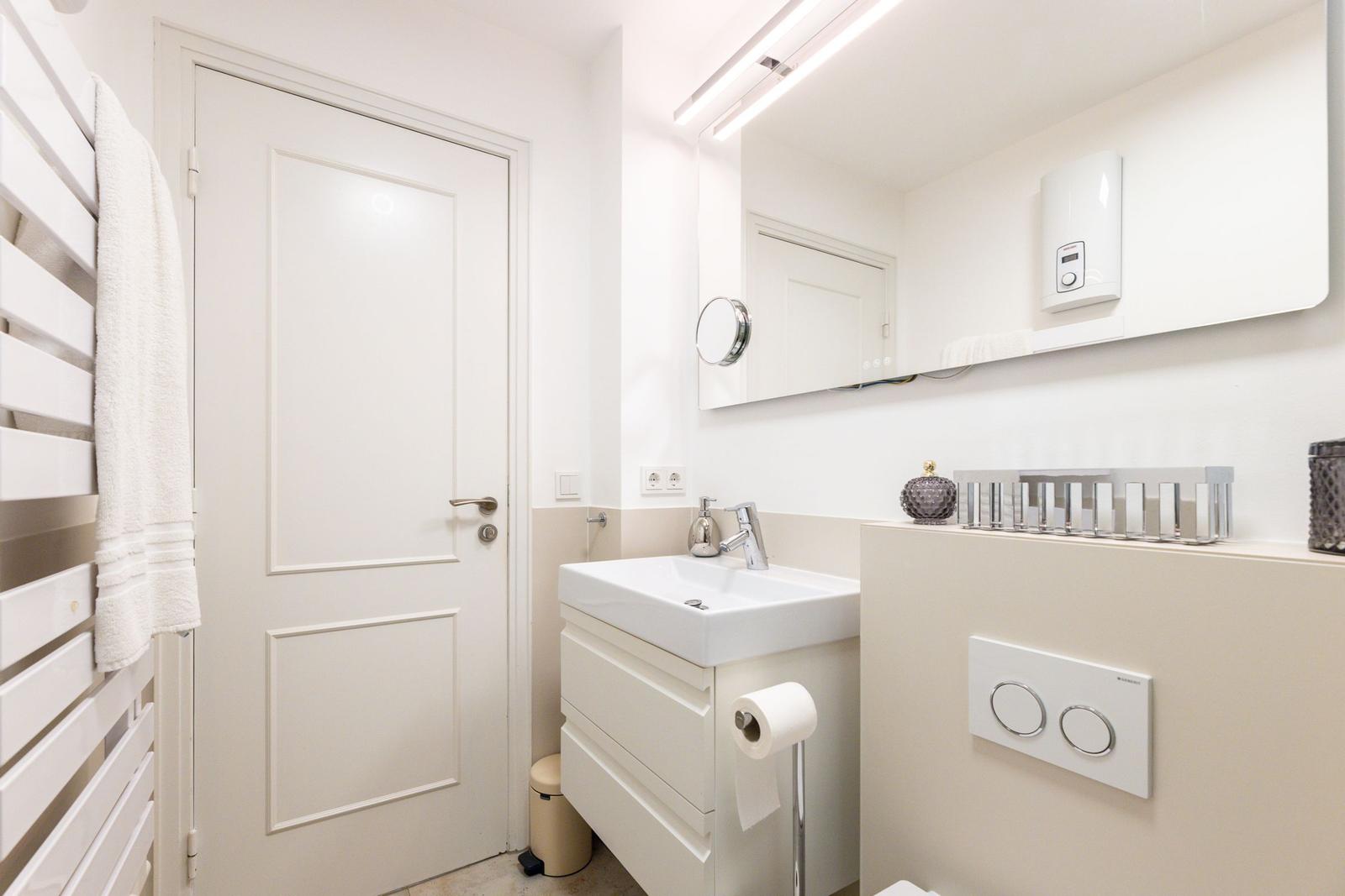 Badezimmer mit Waschbecken, Spiegel und Heizung. Toilette und Handtuchhalter sichtbar.