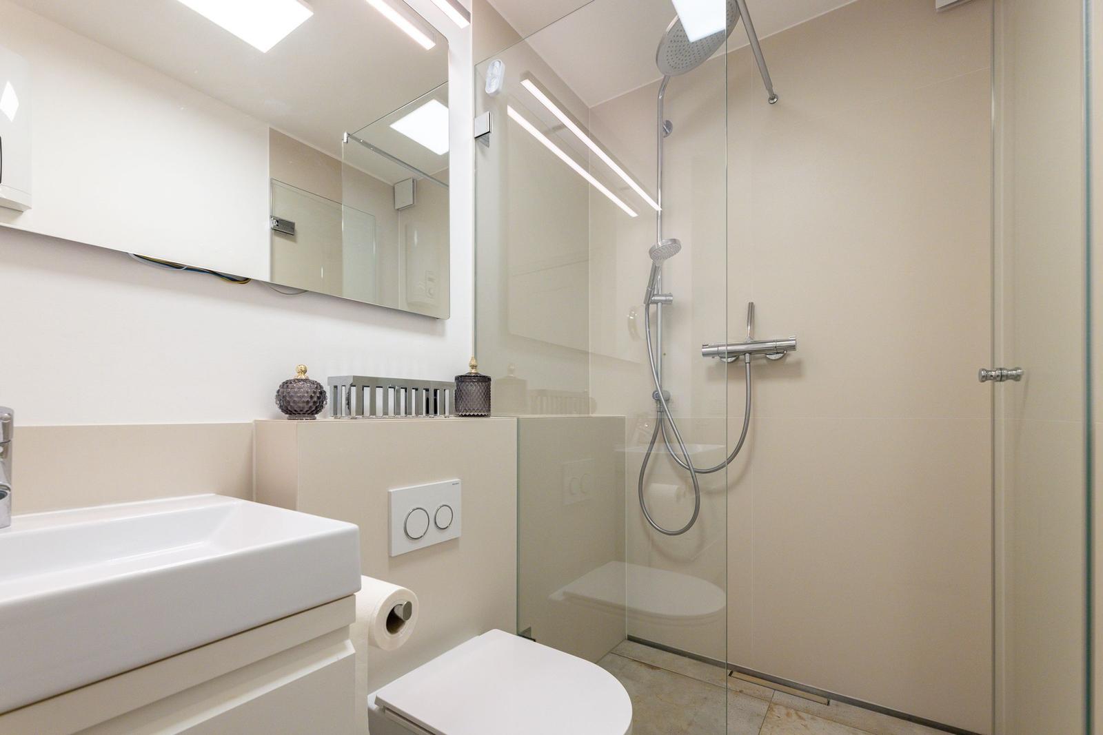 Badezimmer mit Dusche, Waschbecken und Toilette. Moderne Einrichtung mit Spiegel und Licht.
