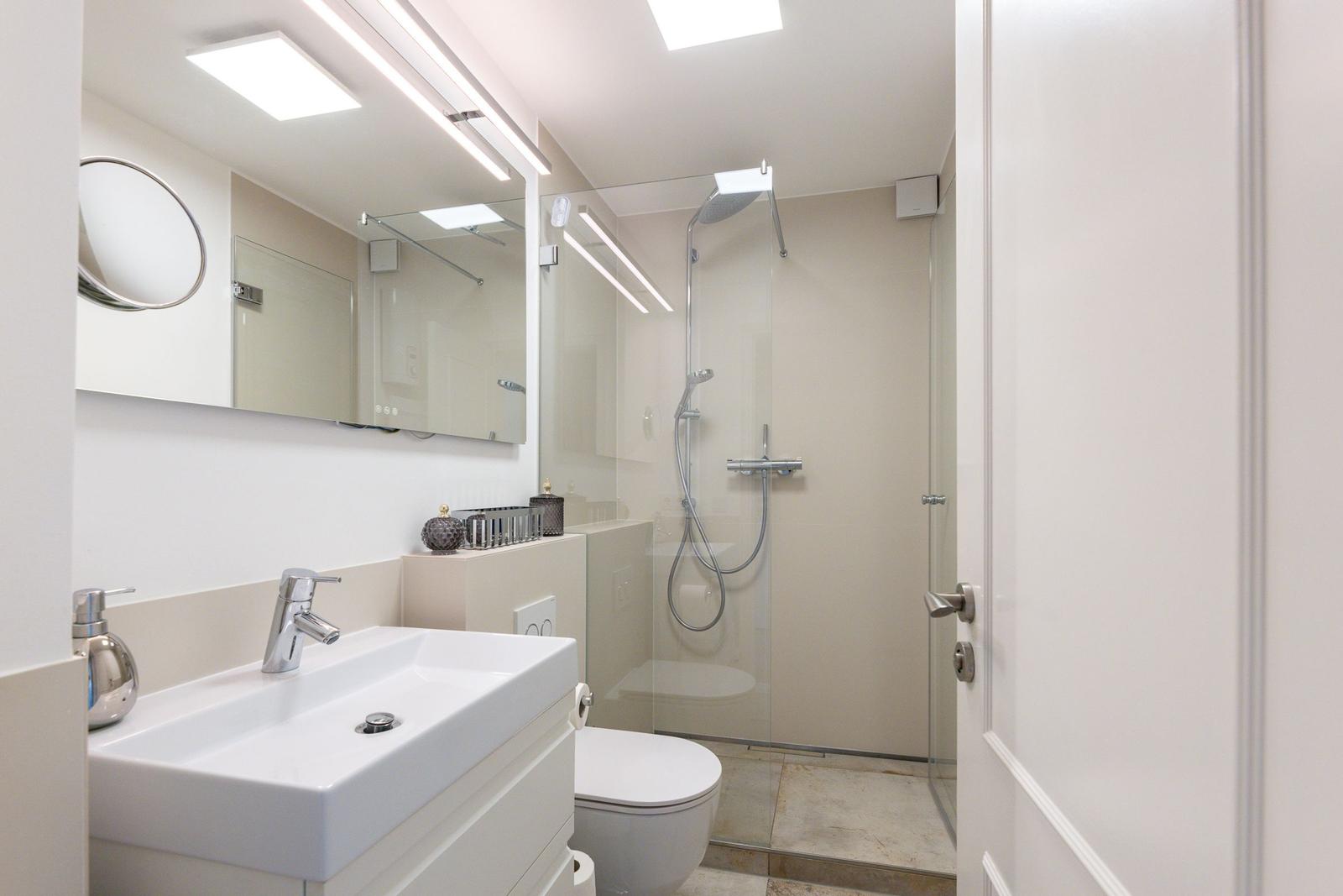 Badezimmer mit Dusche, Waschbecken und Toilette. Moderne Einrichtung mit Spiegel und Beleuchtung.