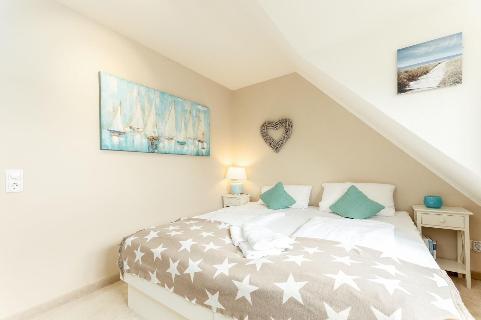 Schlafzimmer mit Dachschrägen, Bett mit Sternen-Decke, zwei Nachttische und Wandbild mit Segelbooten.