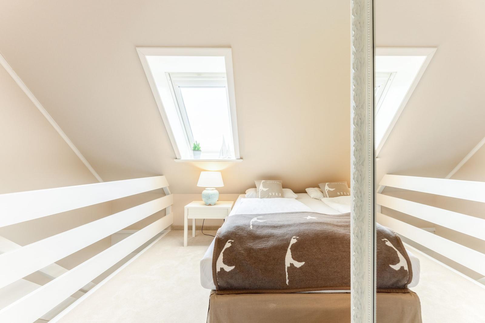 Dachgeschosszimmer mit Dachschrägen, Dachfenster und Bett mit Decke.