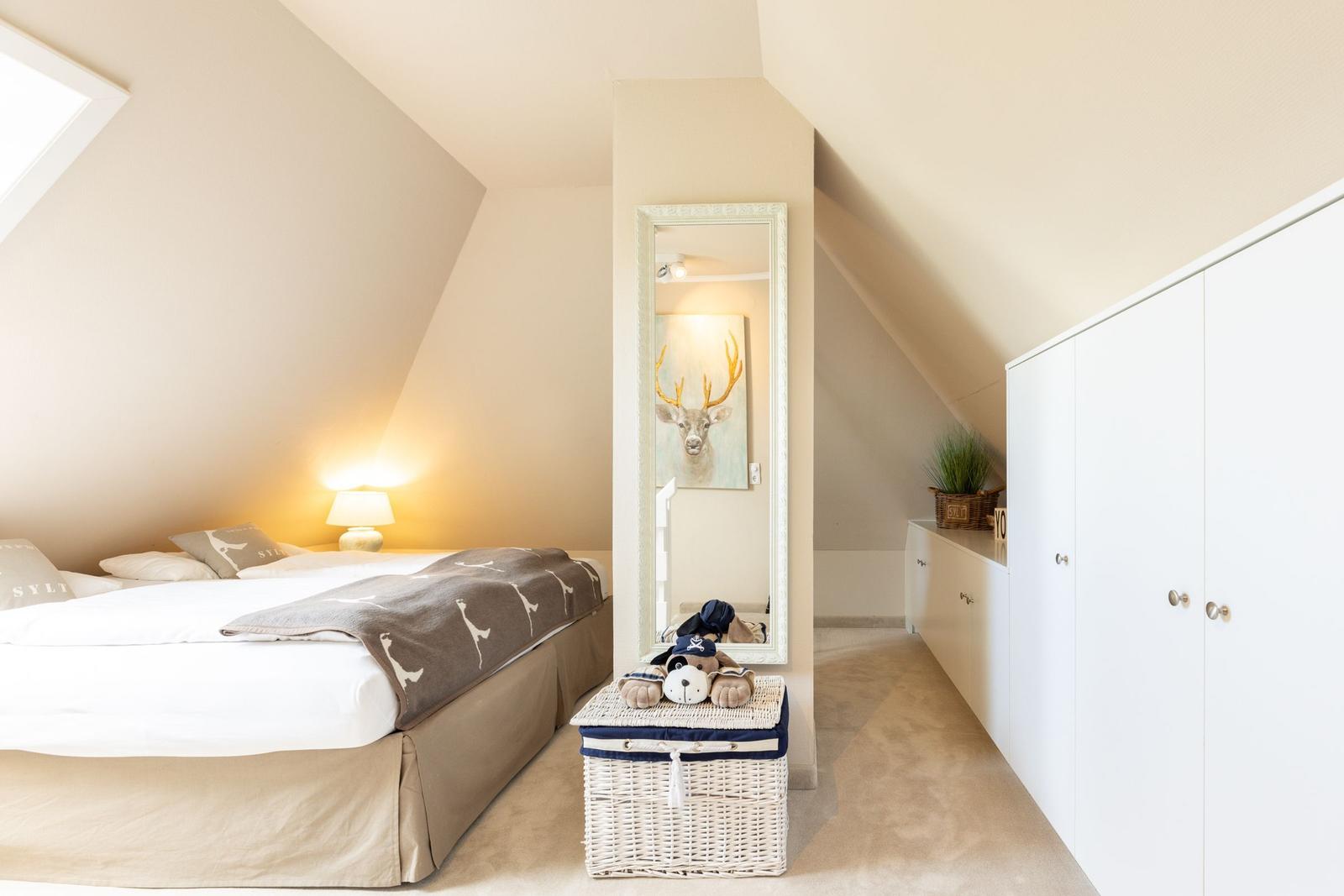 Schlafzimmer mit Dachschrägen, Bett, Spiegel und weißem Schrank.