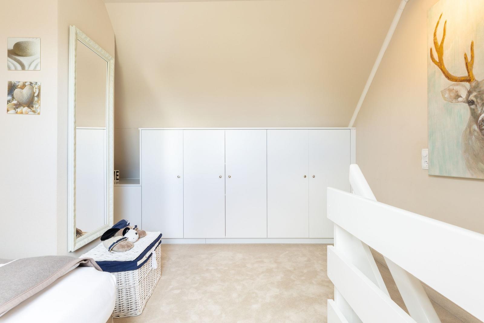 Schlafzimmer mit weißem Schrank, Spiegel und Wandbild mit Hirsch.