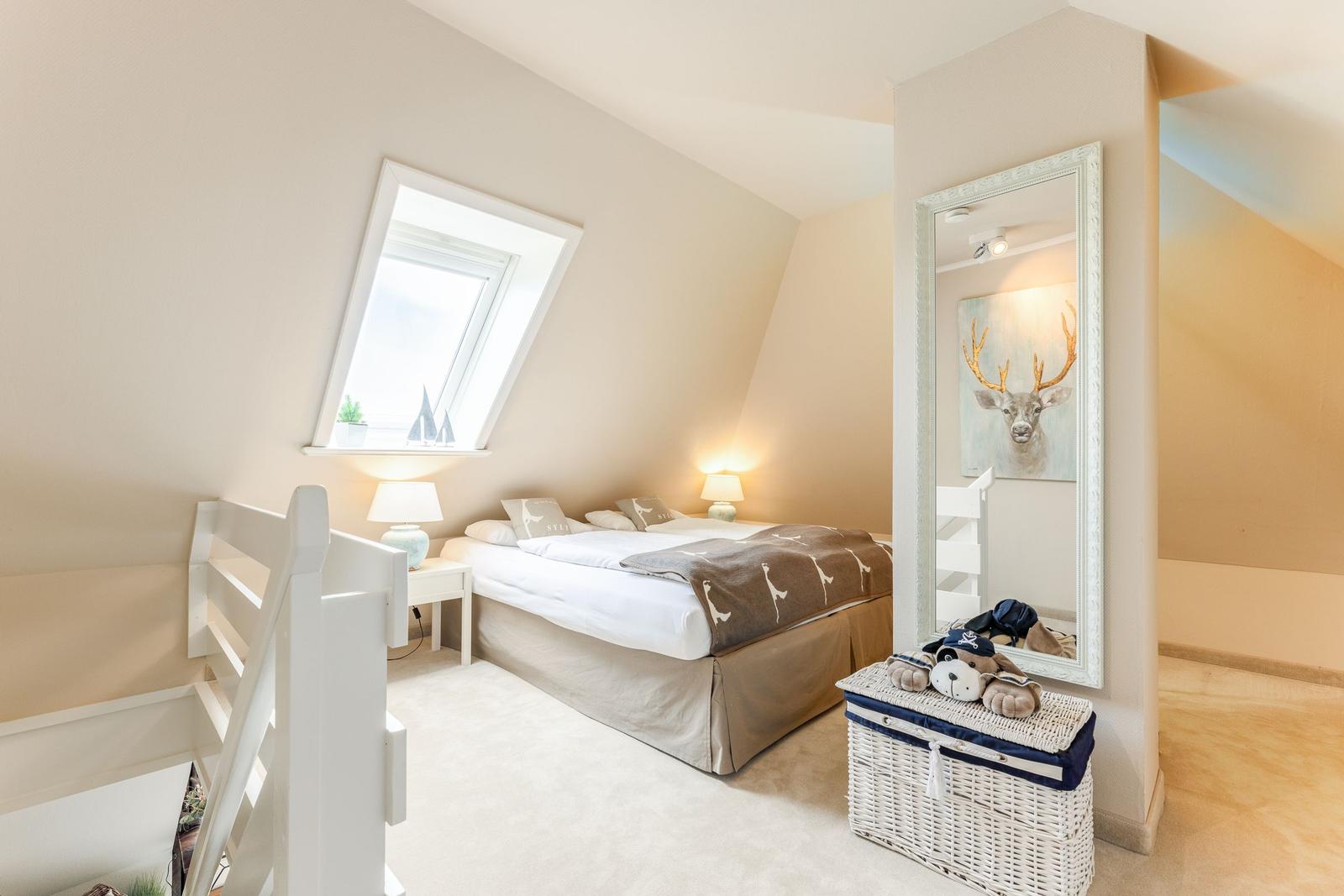 Schlafzimmer mit Dachschräge, Dachfenster, Bett, Spiegel und Korb.