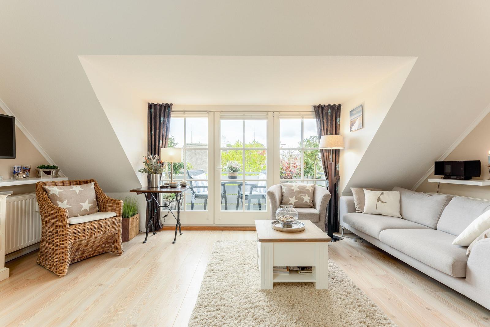 Wohnzimmer mit Sofa, Sessel und Blick auf Balkon.