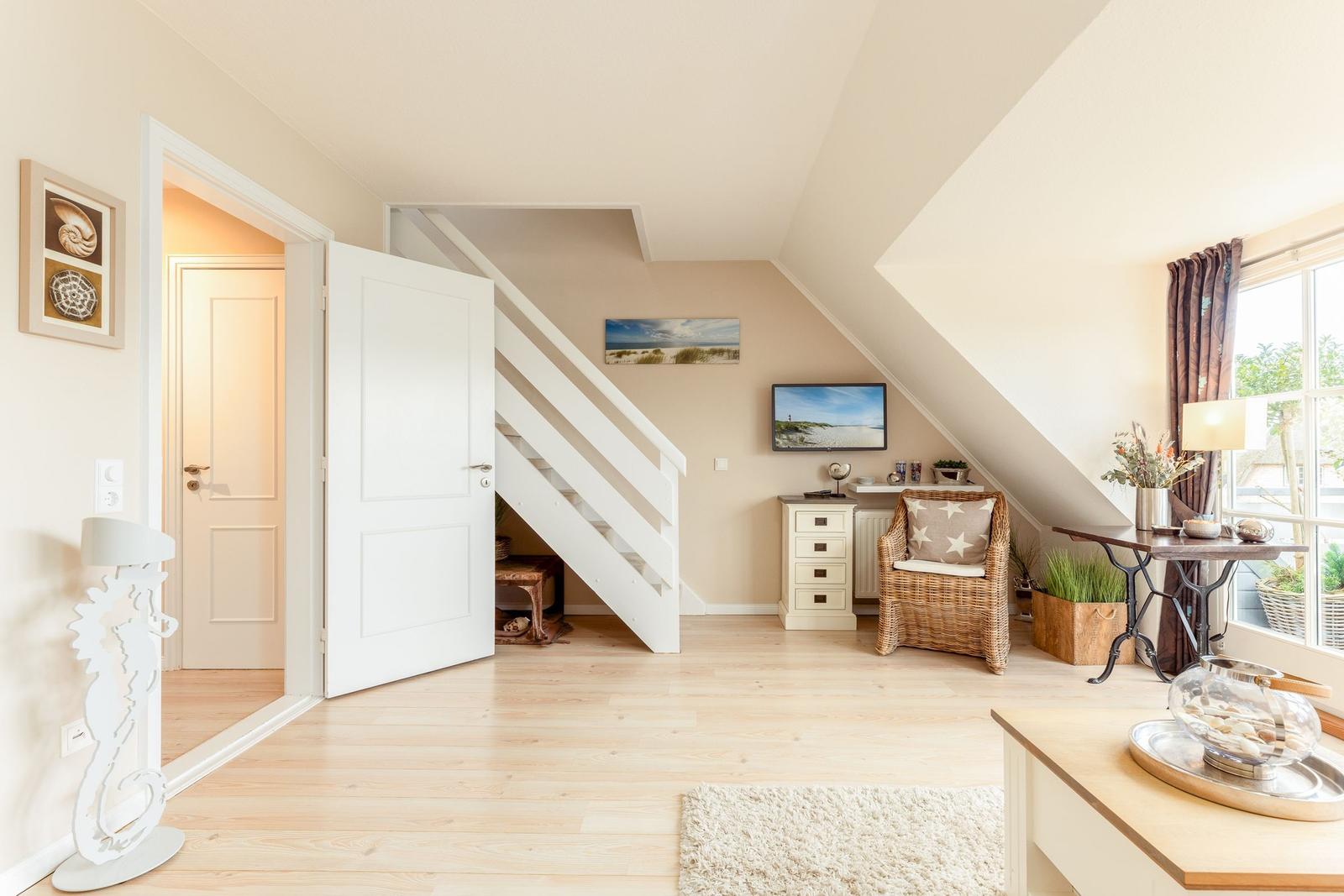 Wohnbereich mit Holzboden, Treppenhaus und Sitzgelegenheit unter Dachschräge.
