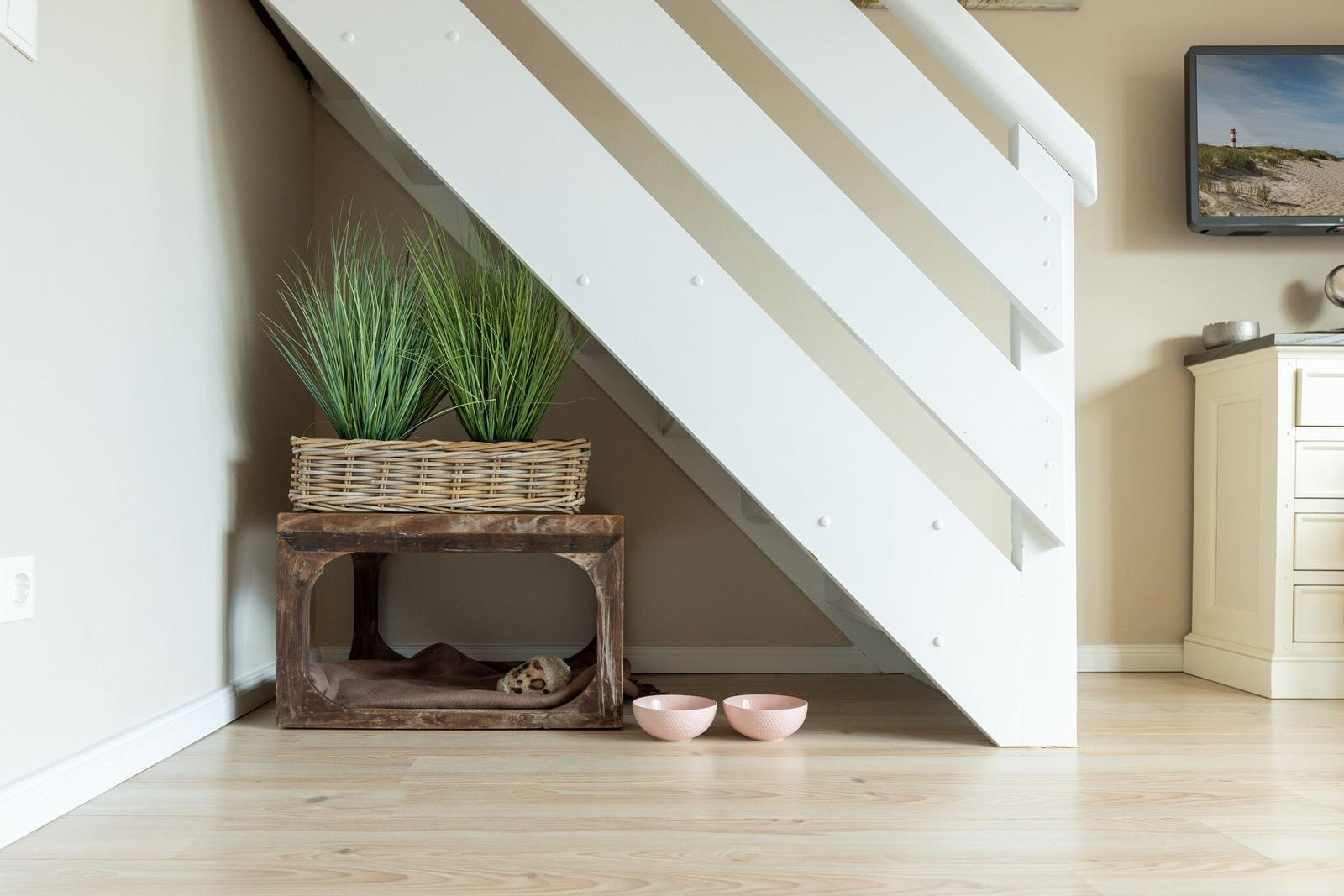 Unter der Treppe steht ein Holzstuhl mit Pflanzen und zwei rosa Schalen.
