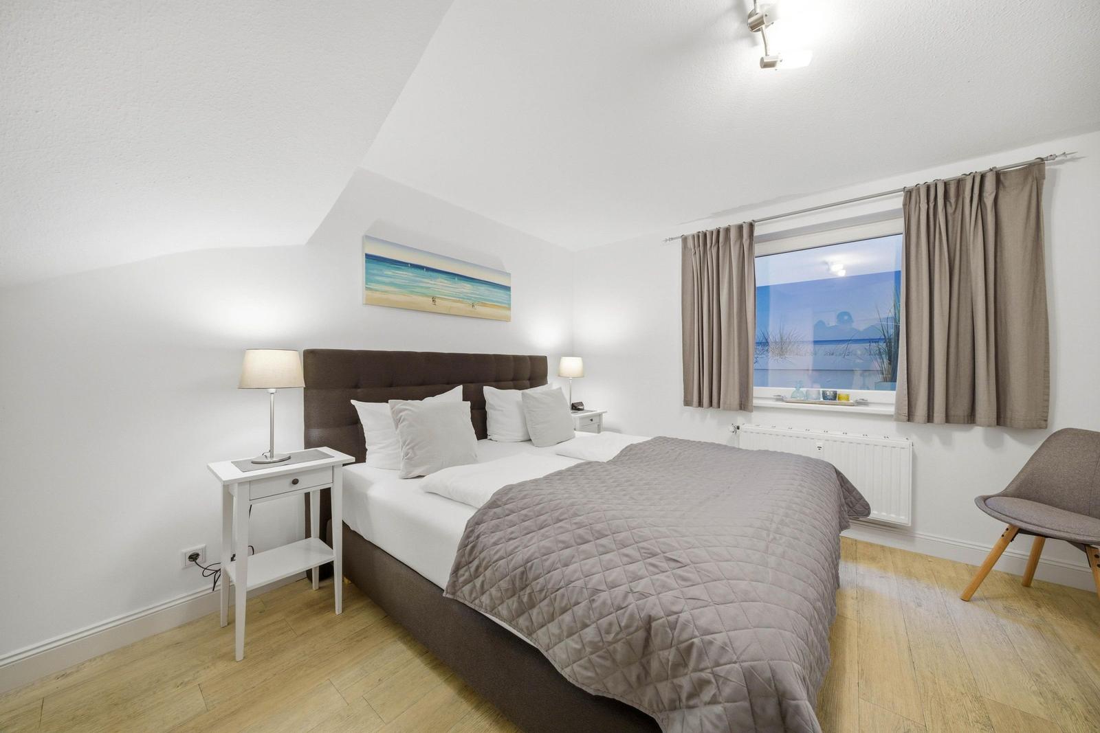 Bedroom with bed, nightstand, and window view of beach.