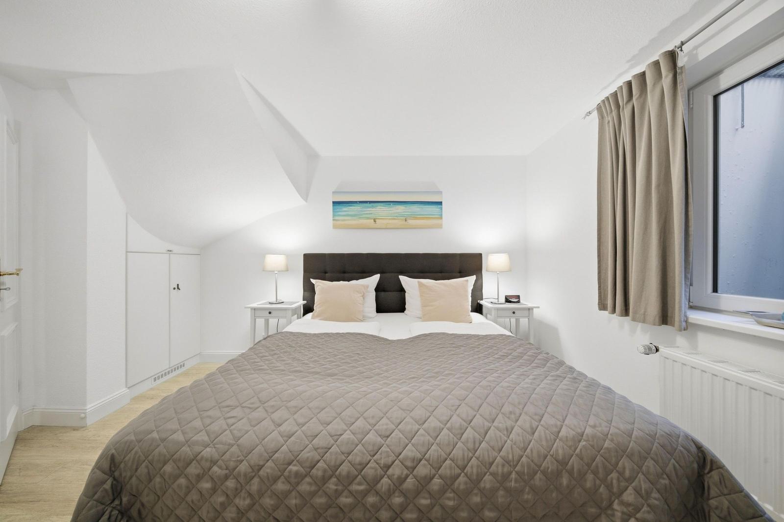 Bedroom with sloped ceiling, bed, nightstands, and window with curtains.