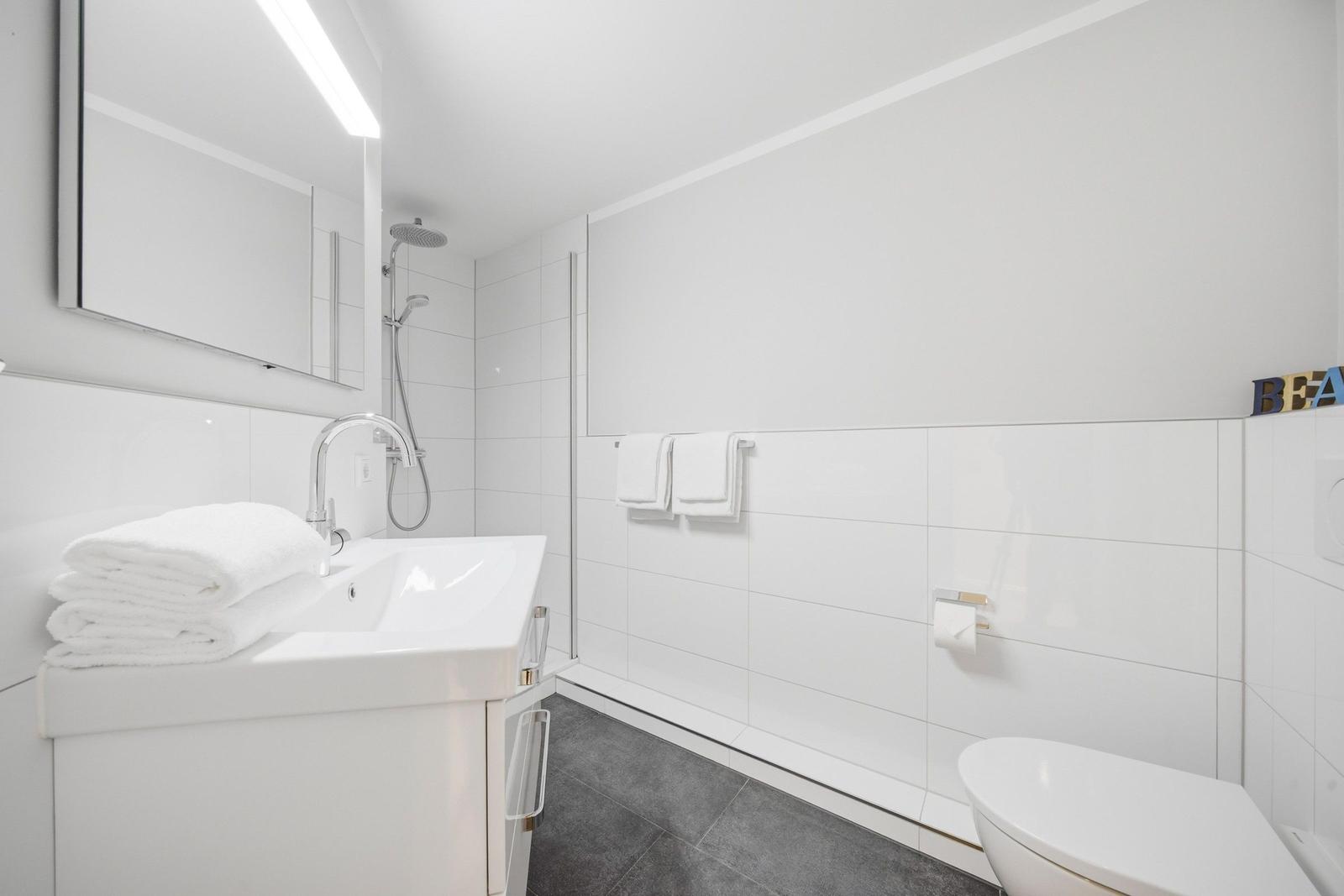 Bathroom with shower, sink, and toilet. White tiles and towels.