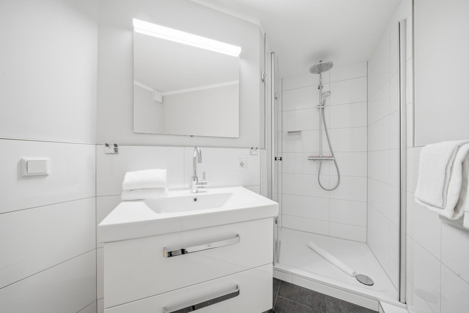 Bathroom with shower, sink, and mirror. White tiles and modern fixtures.