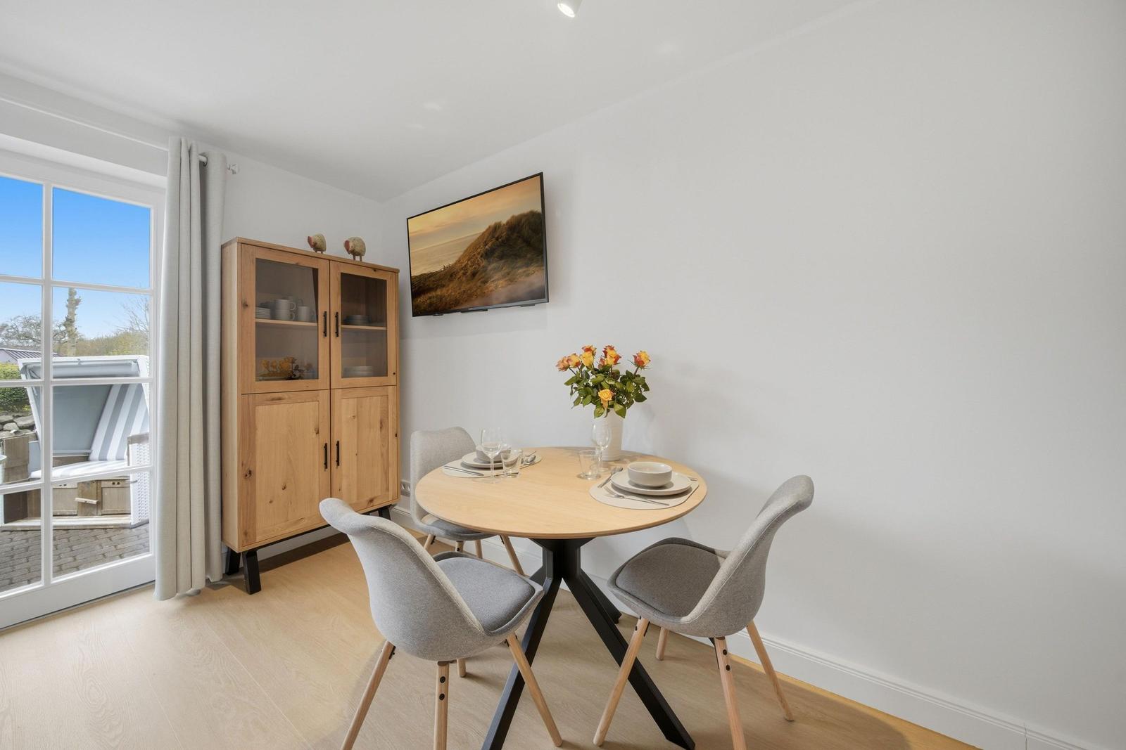 Round table with four chairs, wooden cabinet, and window view.