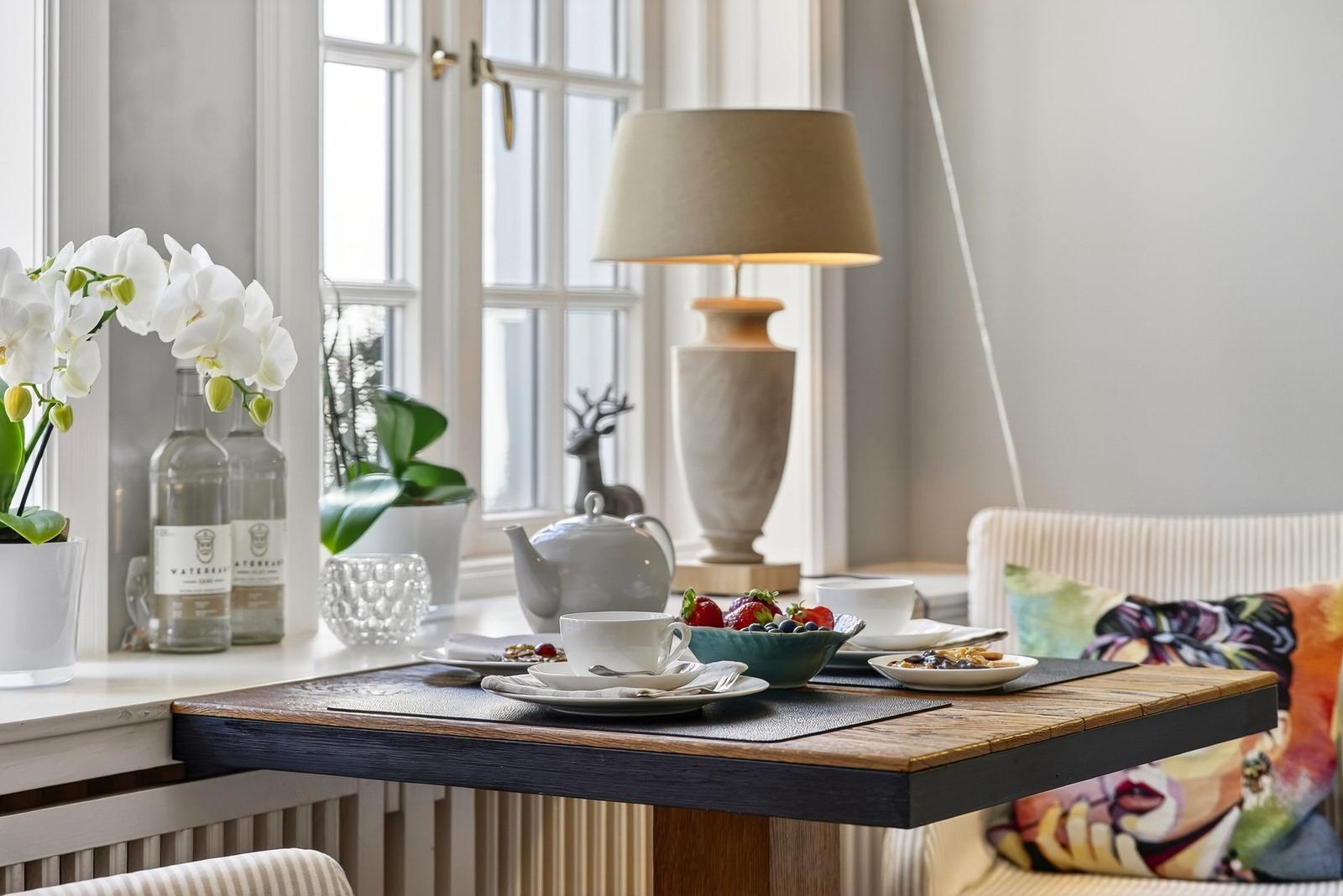 Esstisch mit Tasse, Obst und Lampe vor Fenster