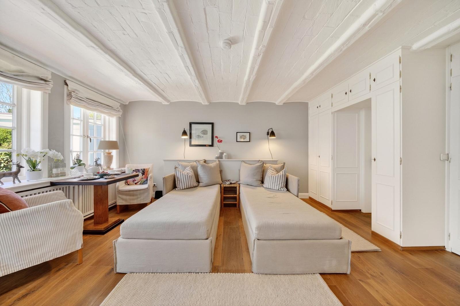 Zwei Schlafsofas mit Kissen stehen im Raum. Holzboden und weiße Deckenbalken sind sichtbar.