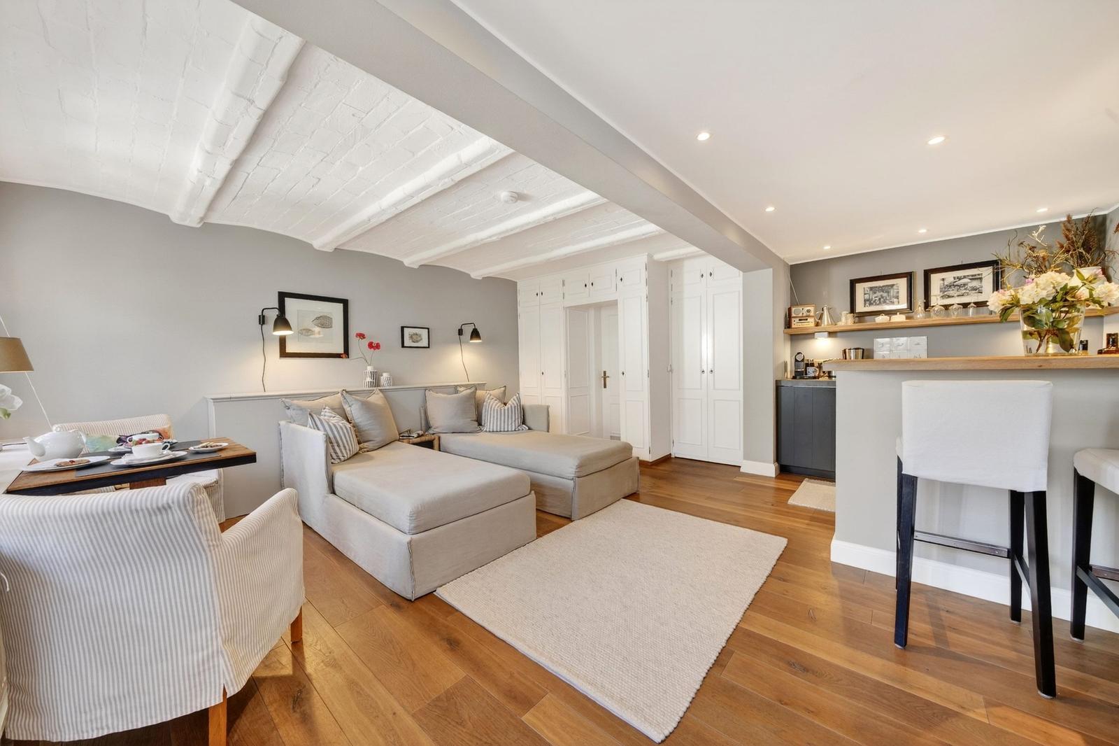 Wohnbereich mit Sofa, Esstisch und Küchenzeile unter weiß gestrichenen Balken.