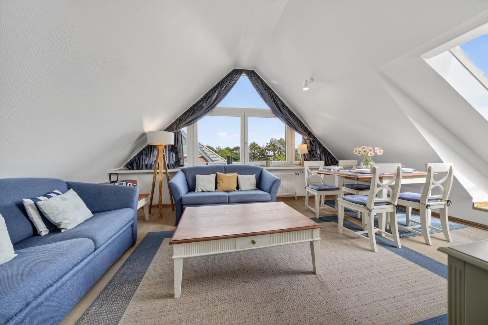 Wohn- und Essbereich mit blauen Sofas, Tisch und Stühlen unter Dachschrägen.