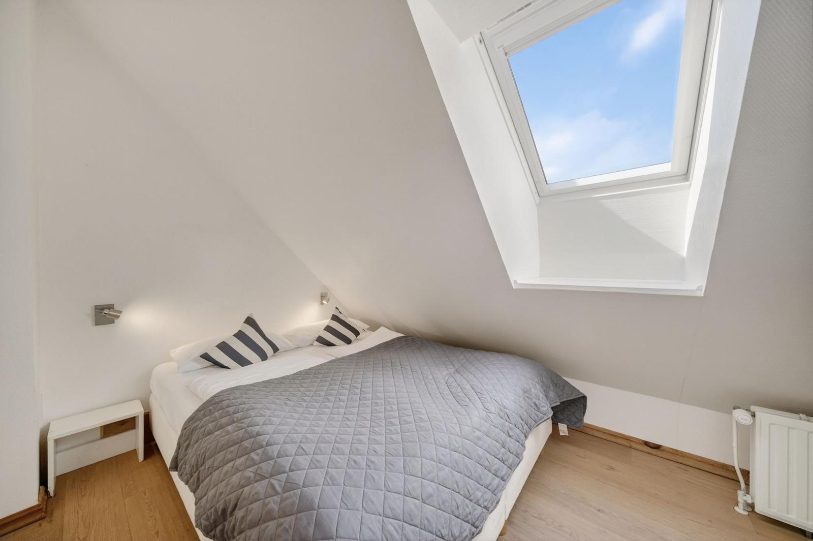 Schlafzimmer mit Dachfenster, Bett, Kissen und Holzboden.