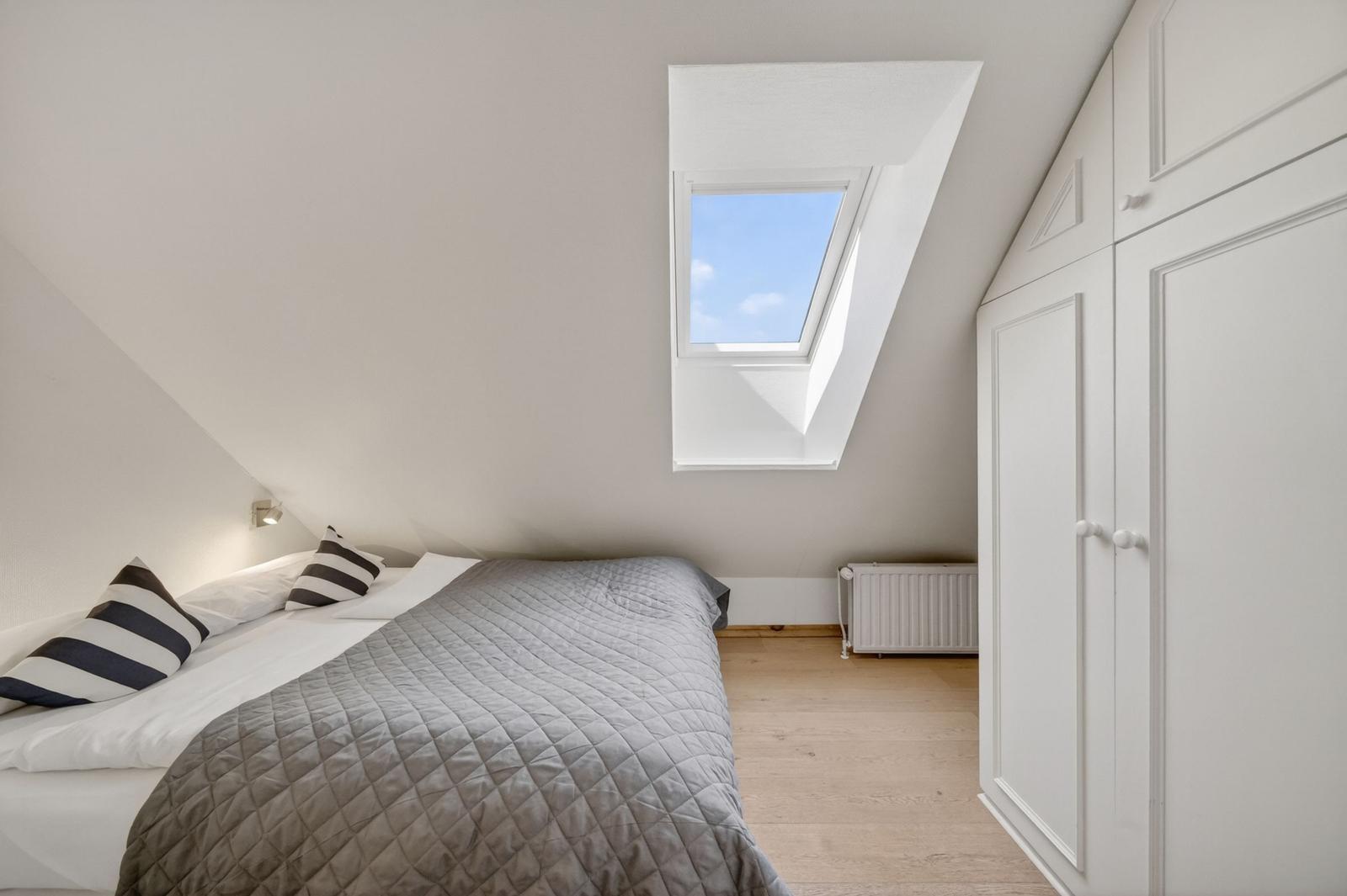 Schlafzimmer mit Dachschrägen, Dachfenster und weißem Schrank.