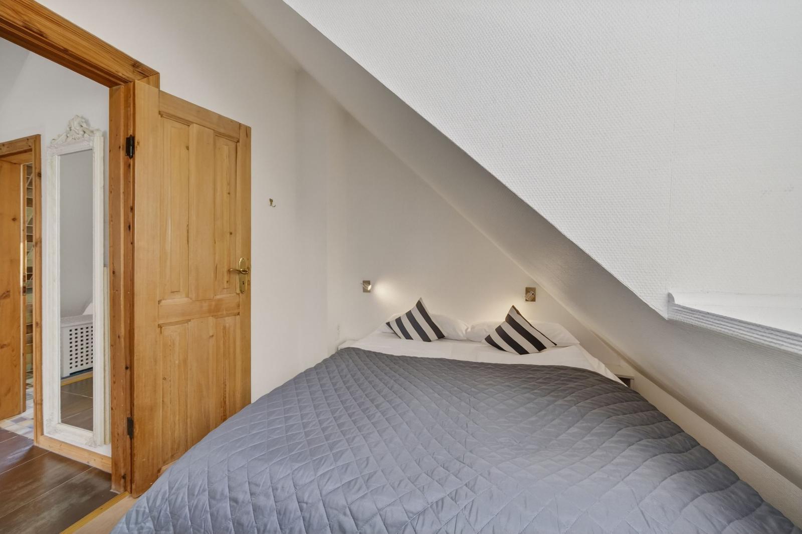Schlafzimmer mit Dachschrägen, Bett mit Kissen und Holztür zu angrenzender Raum.