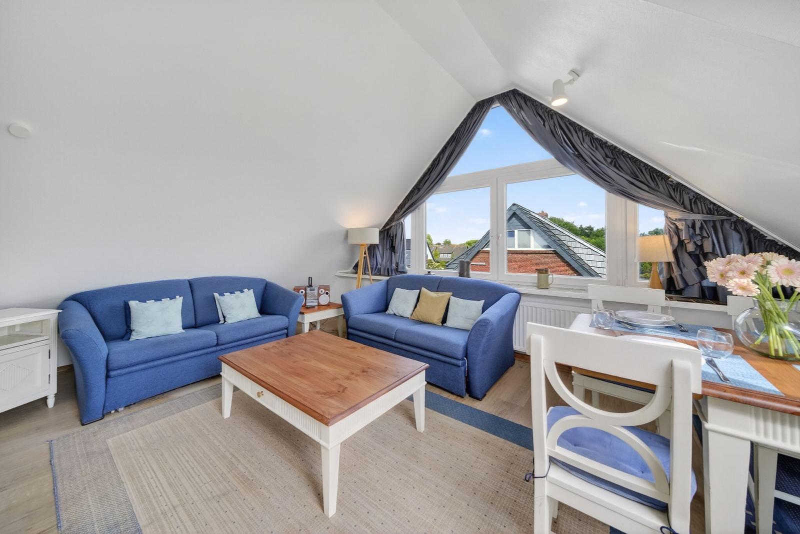 Zimmer mit zwei blauen Sofas, Tisch und Sitzgelegenheiten unter Dachschrägen.