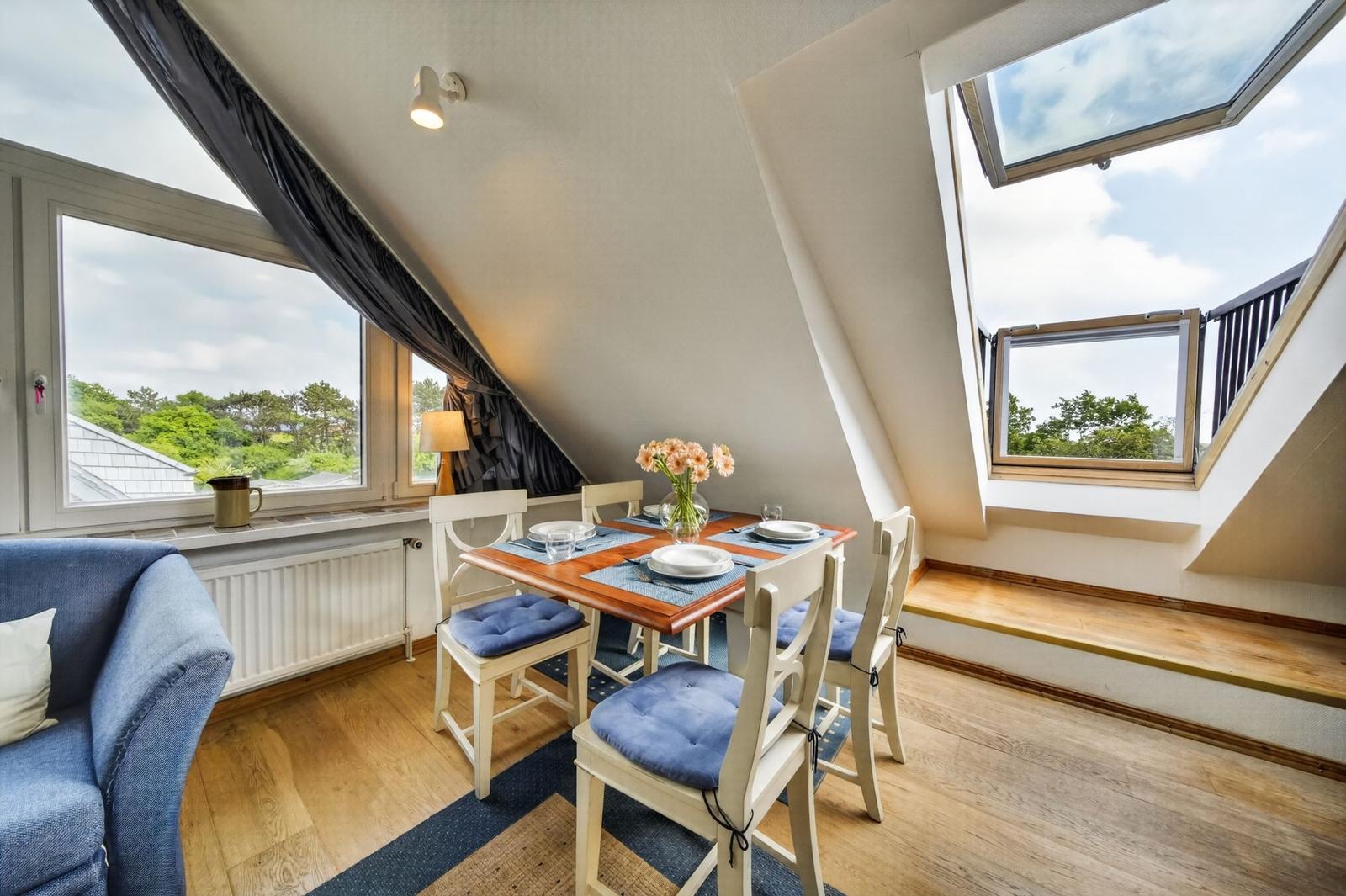 Essbereich mit Tisch, Stühlen und Fenstern. Blick auf grüne Bäume und Himmel.