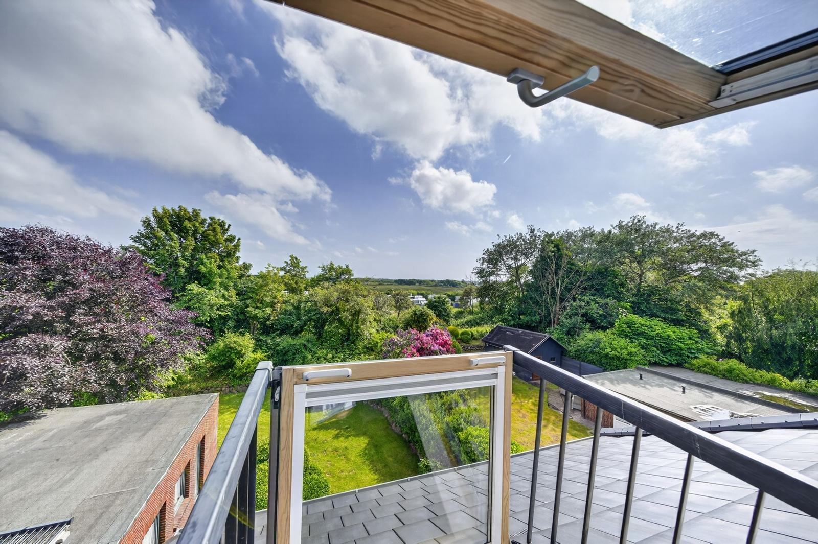 Terrasse mit Blick auf grüne Bäume und einen blauen Himmel mit weißen Wolken.