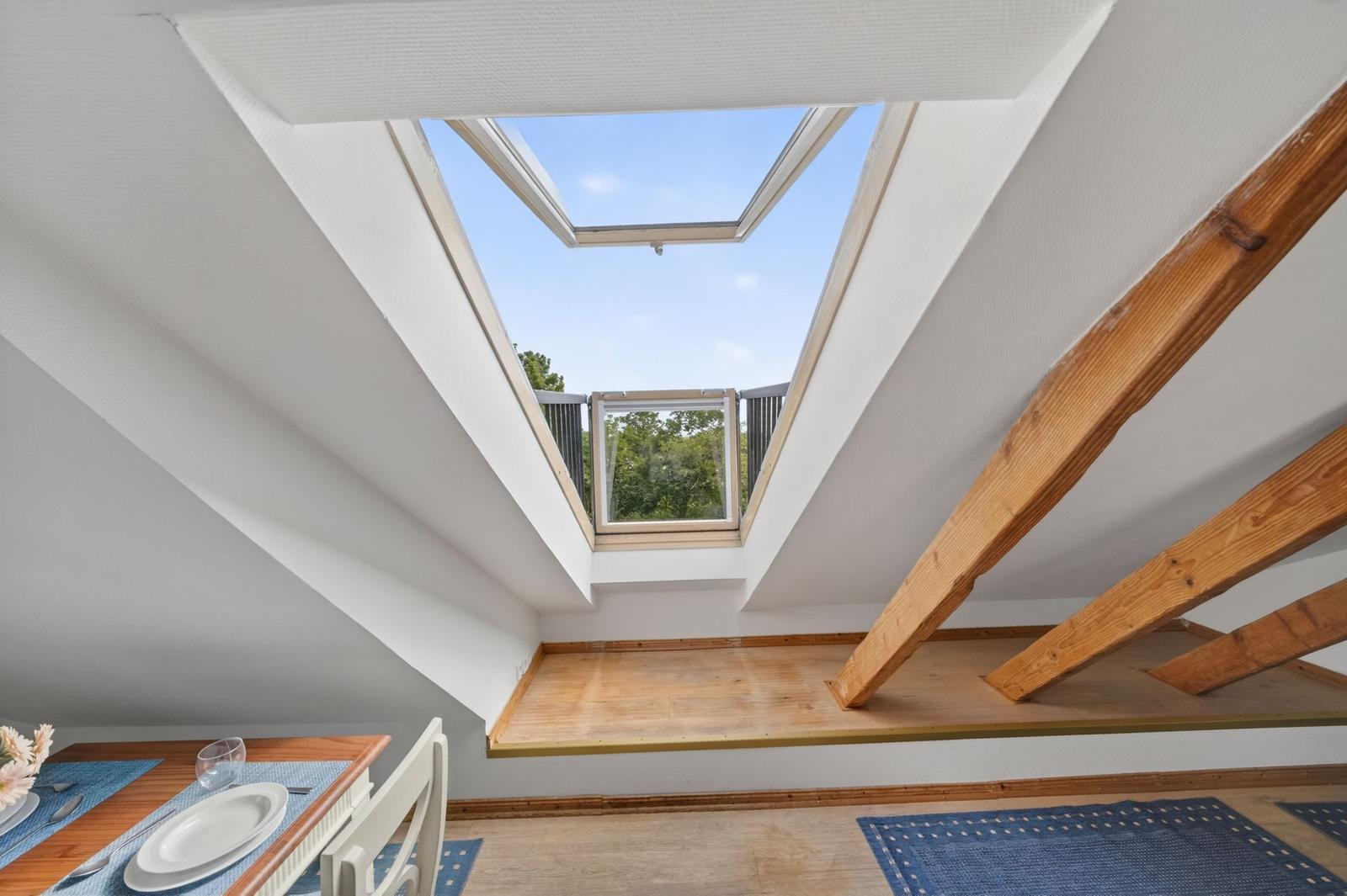 Dachgeschoss mit Satteldach, Holzbalken und Dachfenster mit Blick auf Bäume.