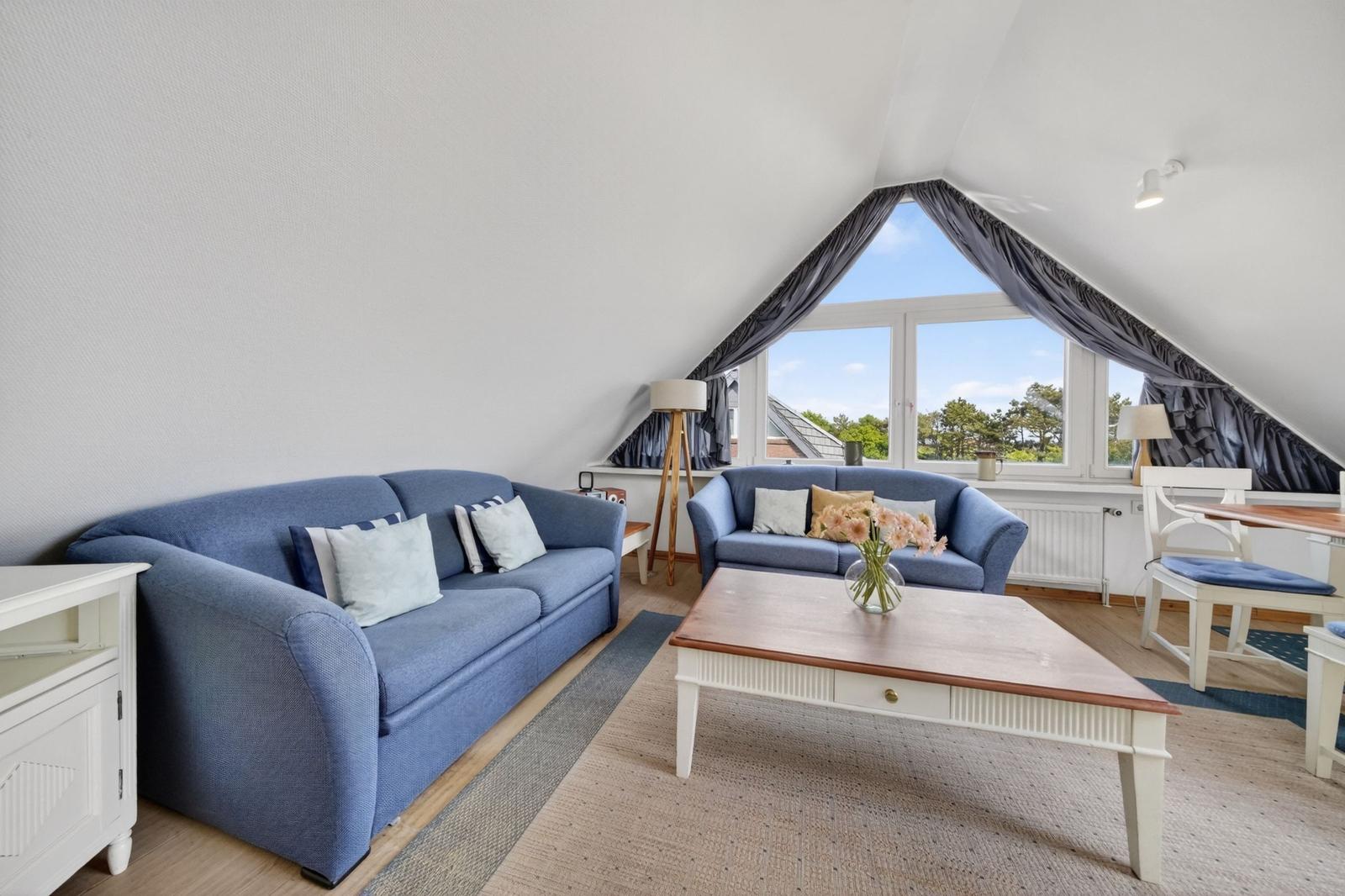 Wohnbereich mit blauen Sofas, Holztisch und großem Dachfenster mit Blick.
