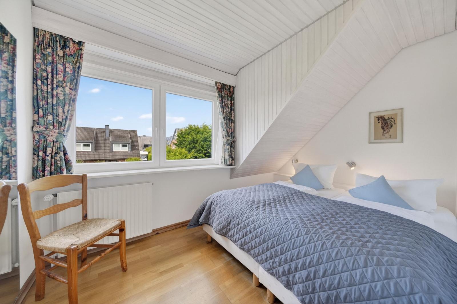Schlafzimmer mit Dachschrägen, Bett, Stuhl und Fenster mit Blick.