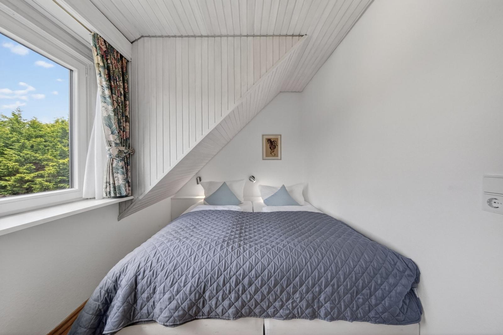 Schlafzimmer mit Dachschräge, Bett und Fenster mit Blick auf Bäume.