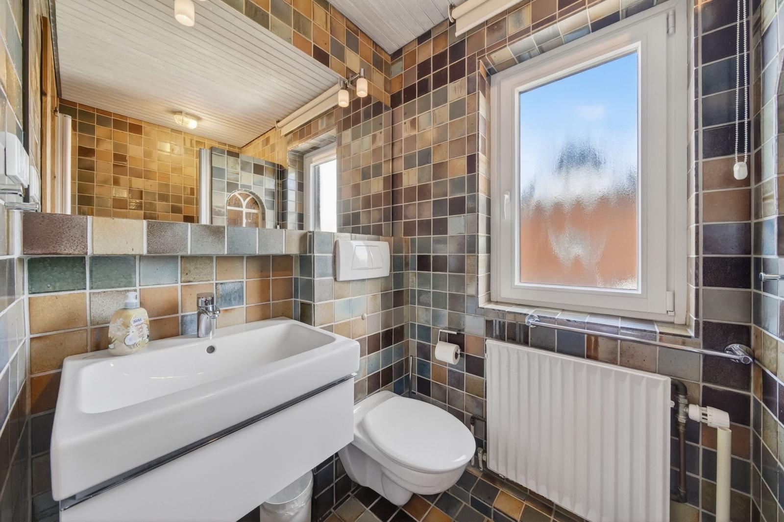 Badezimmer mit Waschbecken, Toilette und Fenster mit getöntem Glas.
