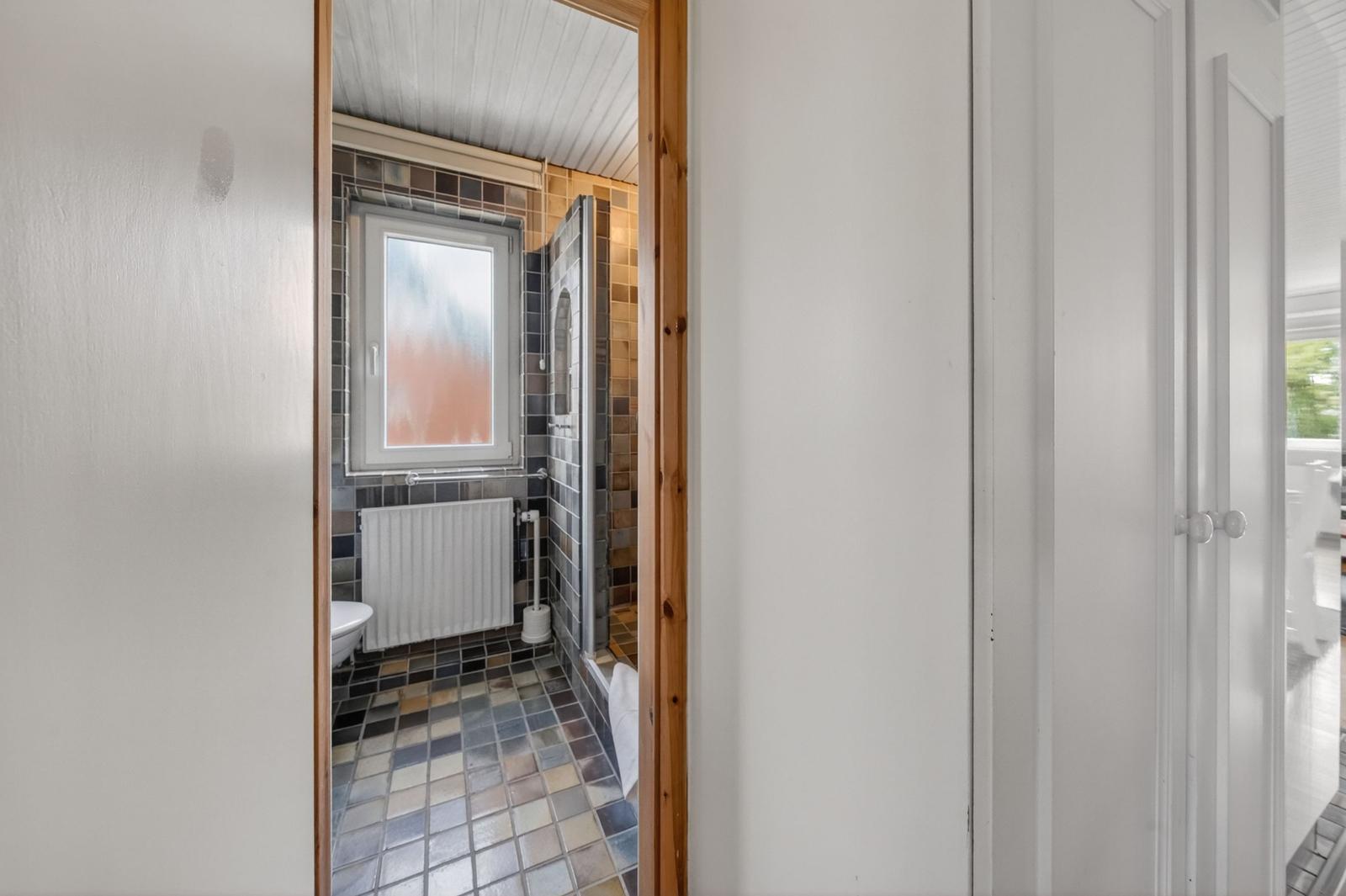 Badezimmer mit gefliestem Boden, Fenster und Dusche.