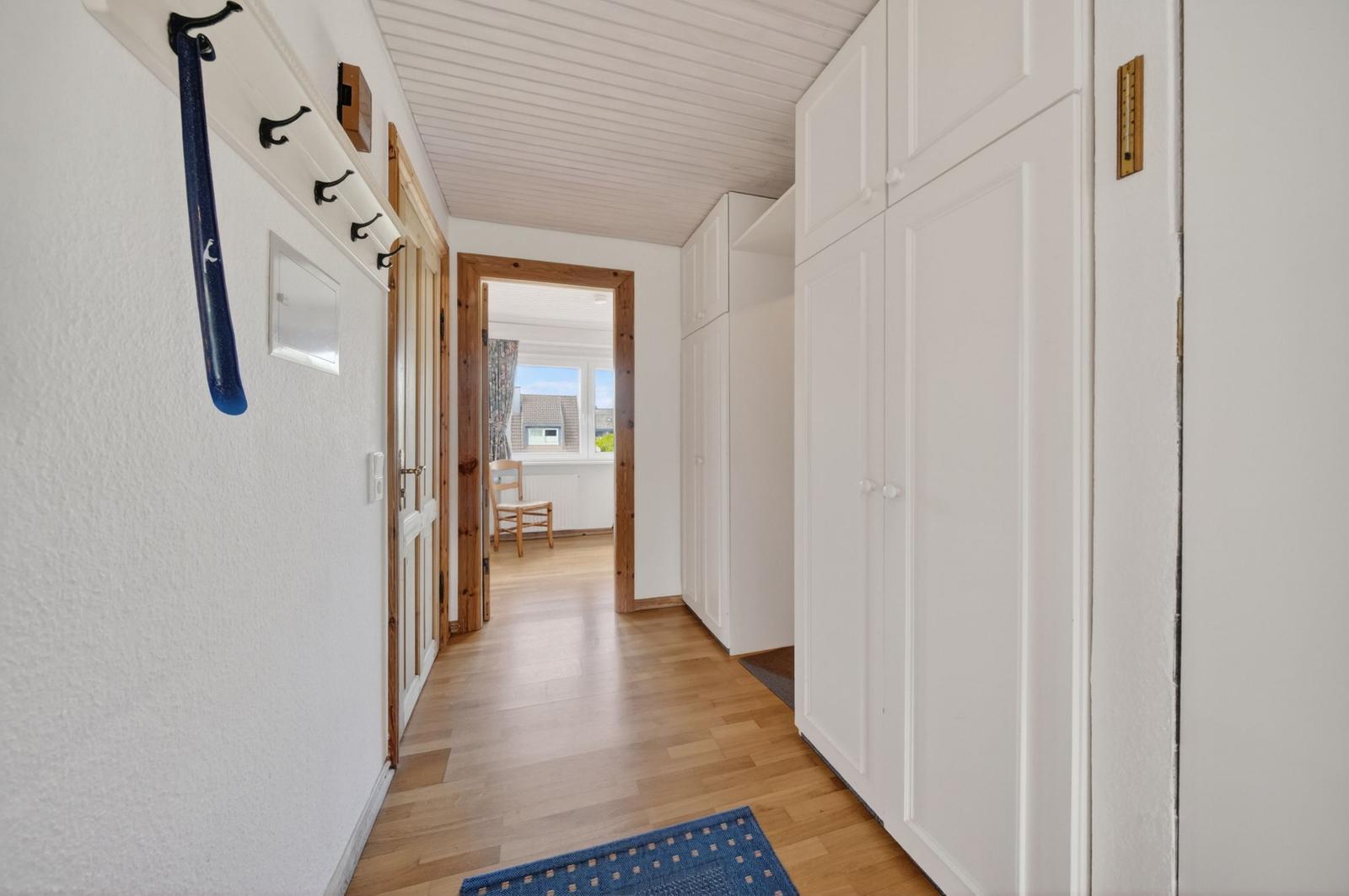 Flur mit weißen Schränken, Holzboden und Sicht auf Wohnzimmer.