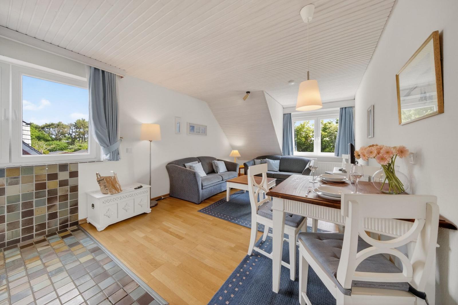 Wohn- und Essbereich mit Sofa, Tisch und Stühlen. Holzboden und Fenster mit Blick.