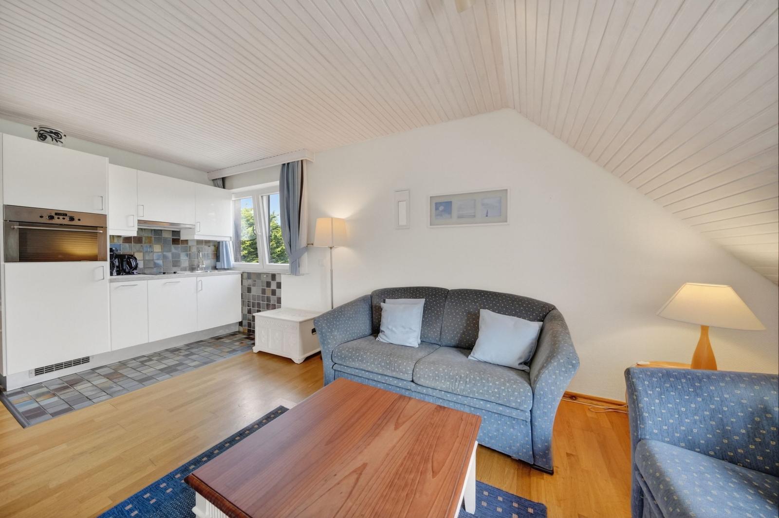 Wohnbereich mit Sofa, Tisch und Küchenzeile unter schrägen Decken.