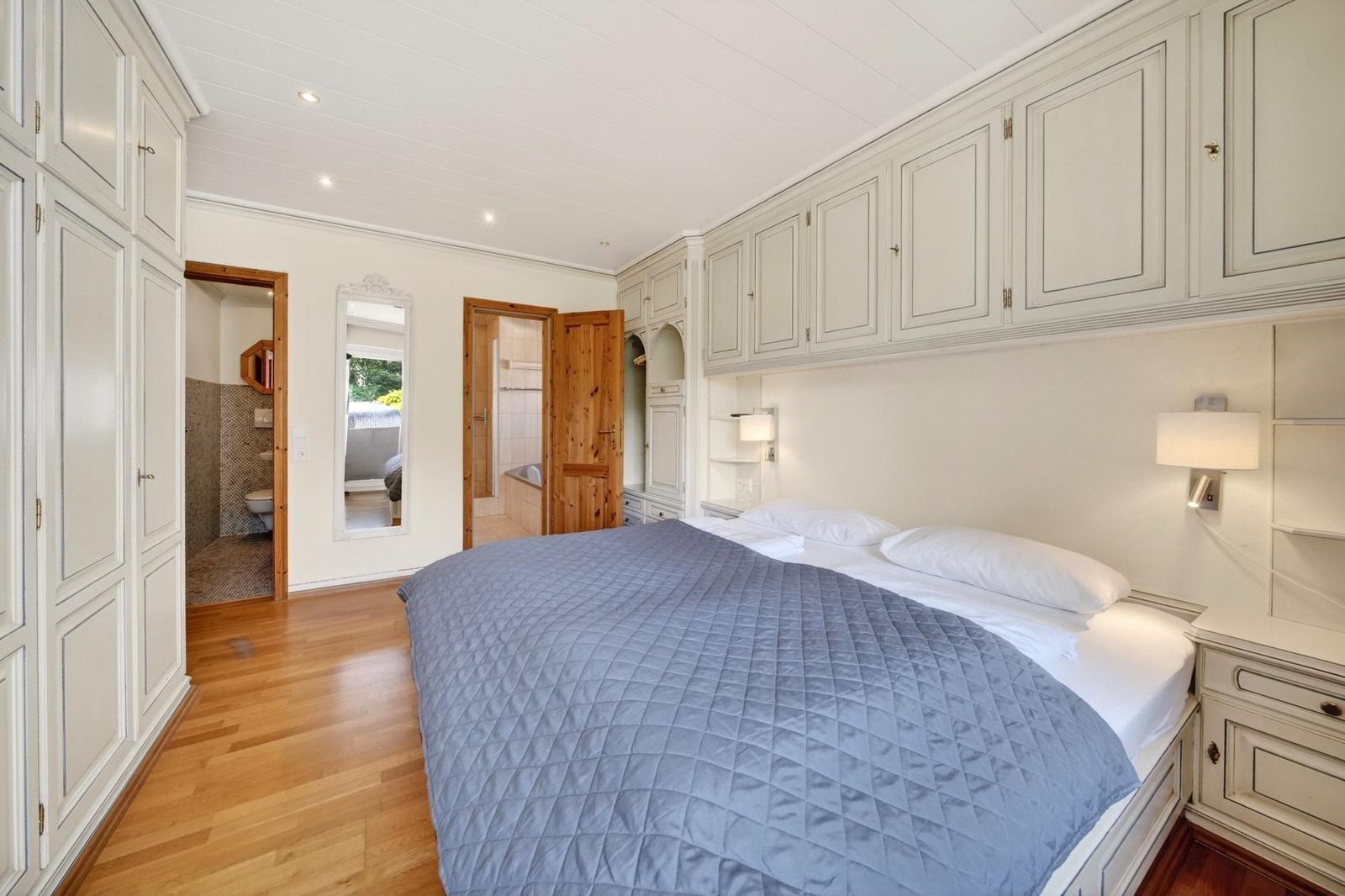 Schlafzimmer mit Bett, Schränken und Holzboden. Durchgänge zu Bad und Dusche.