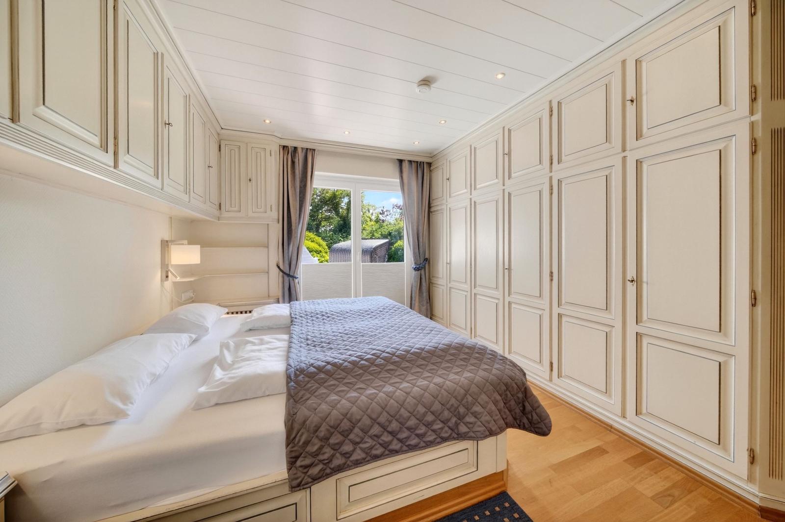 Schlafzimmer mit Bett, Kleiderschrank und Fenster zum Balkon.