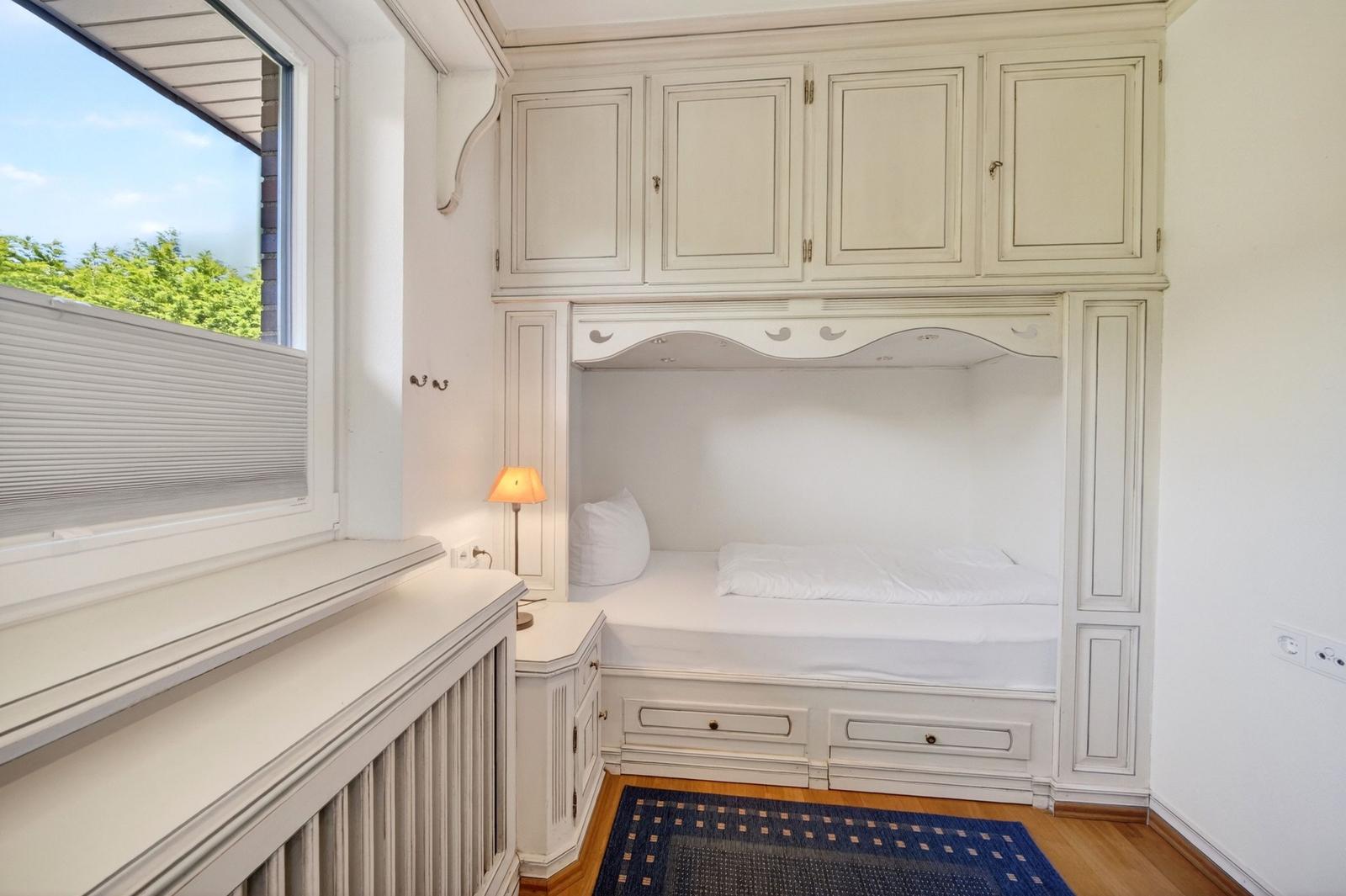 Schlafzimmer mit eingebautem Bett, Schränken und Fenster mit Blick auf Grün.