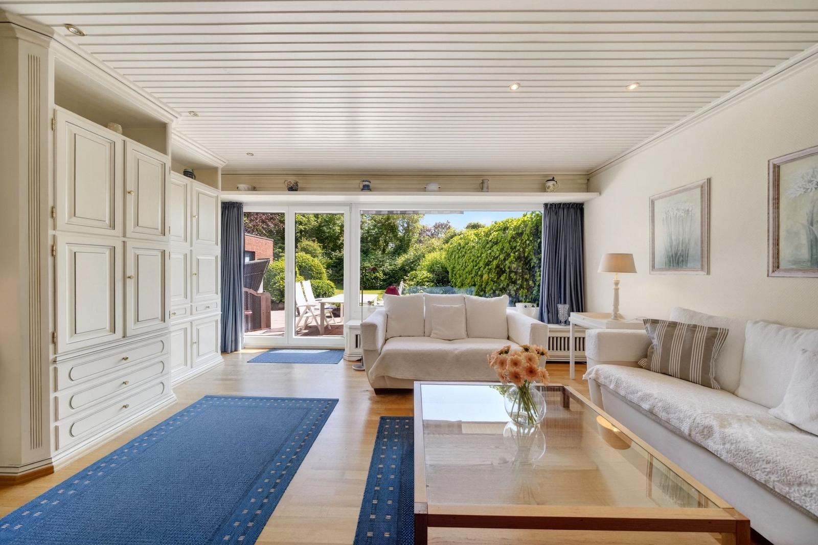 Wohnzimmer mit weißen Sofas, Glas-Tisch und Blick auf den Garten.