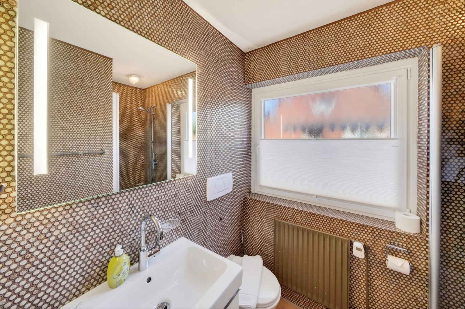 Badezimmer mit Waschbecken, Spiegel und Dusche. Wandverkleidung mit Mosaikfliesen.