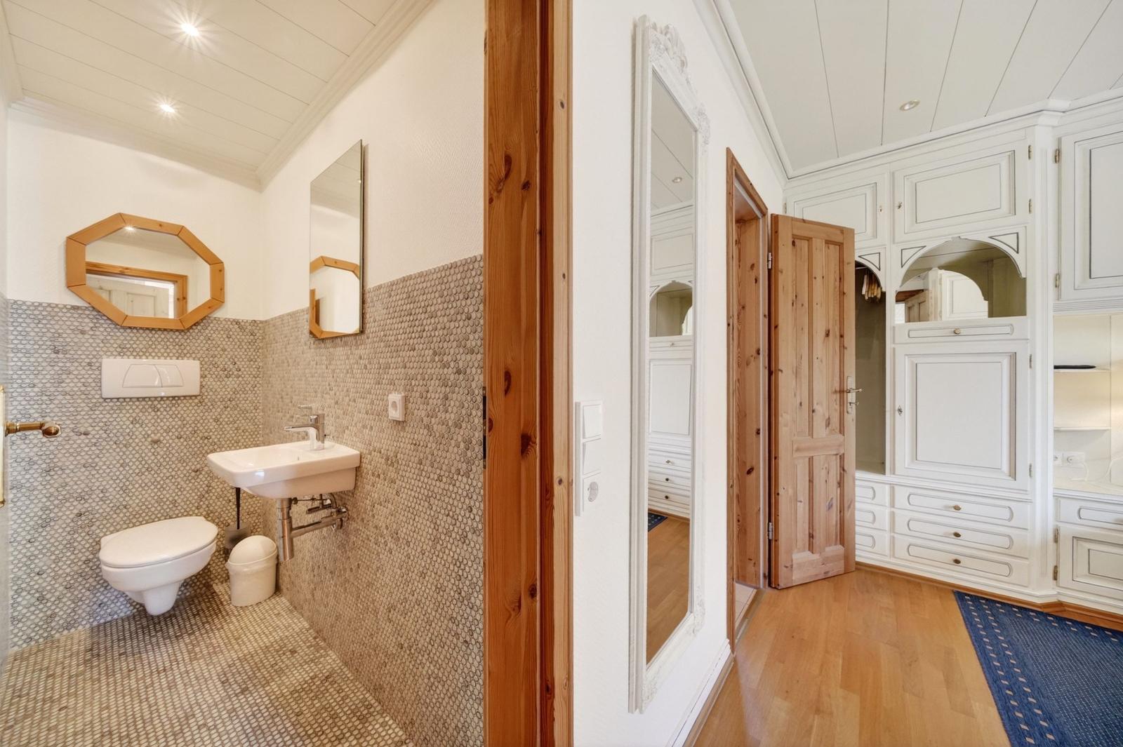 Badezimmer mit Mosaikwand und Toilette. Flur mit Schrank und Holztür.