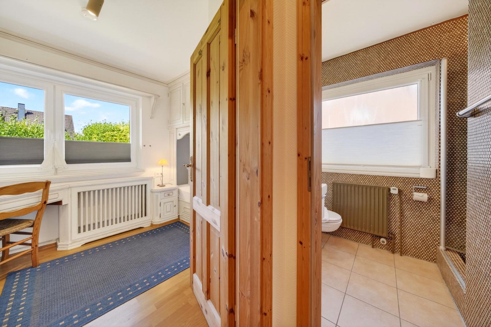 Schlafzimmer mit Schreibtisch und Fenster. Nebenraum mit Toilette und Dusche.
