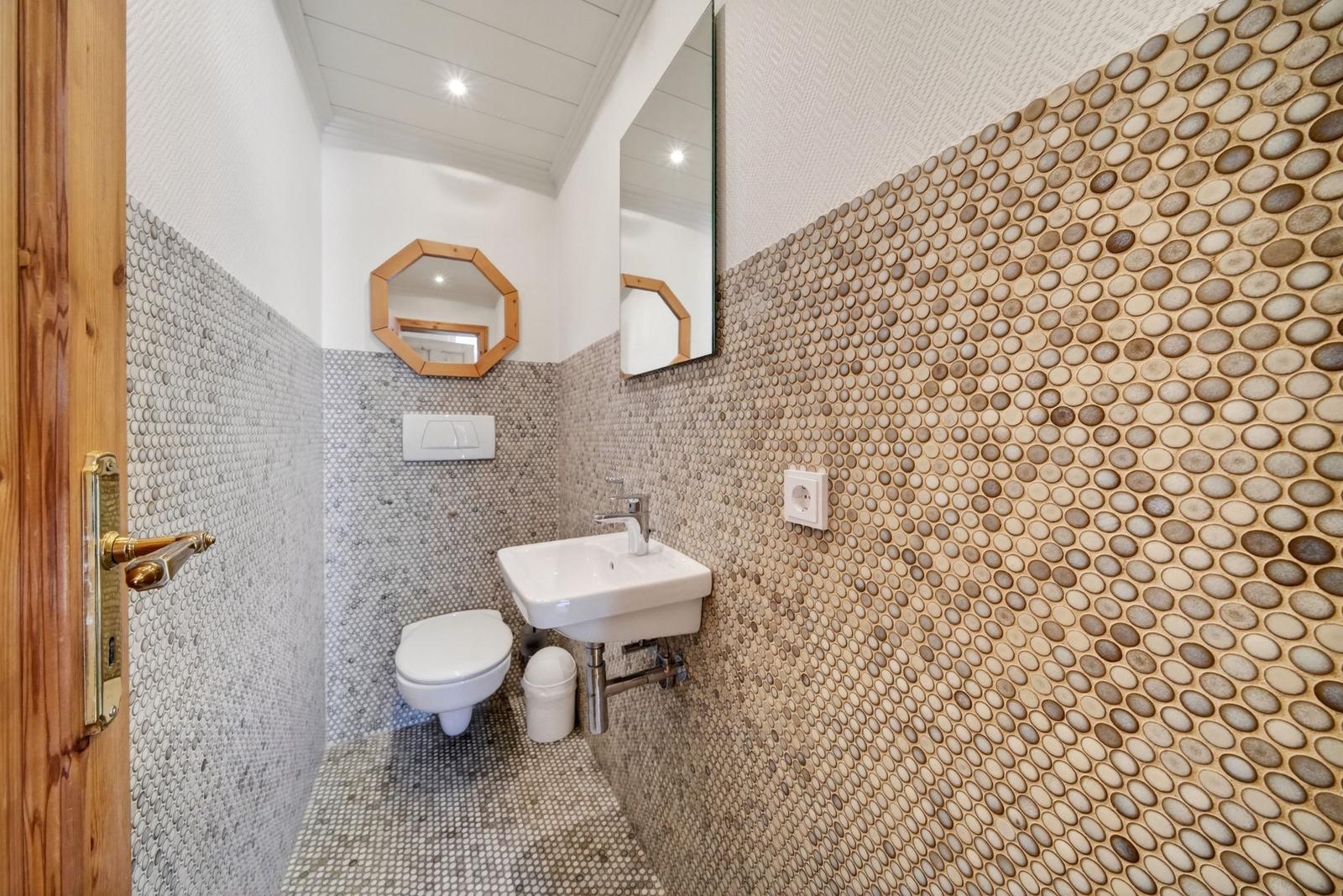 Badezimmer mit Steinwand, Waschbecken, Toilette und Spiegel
