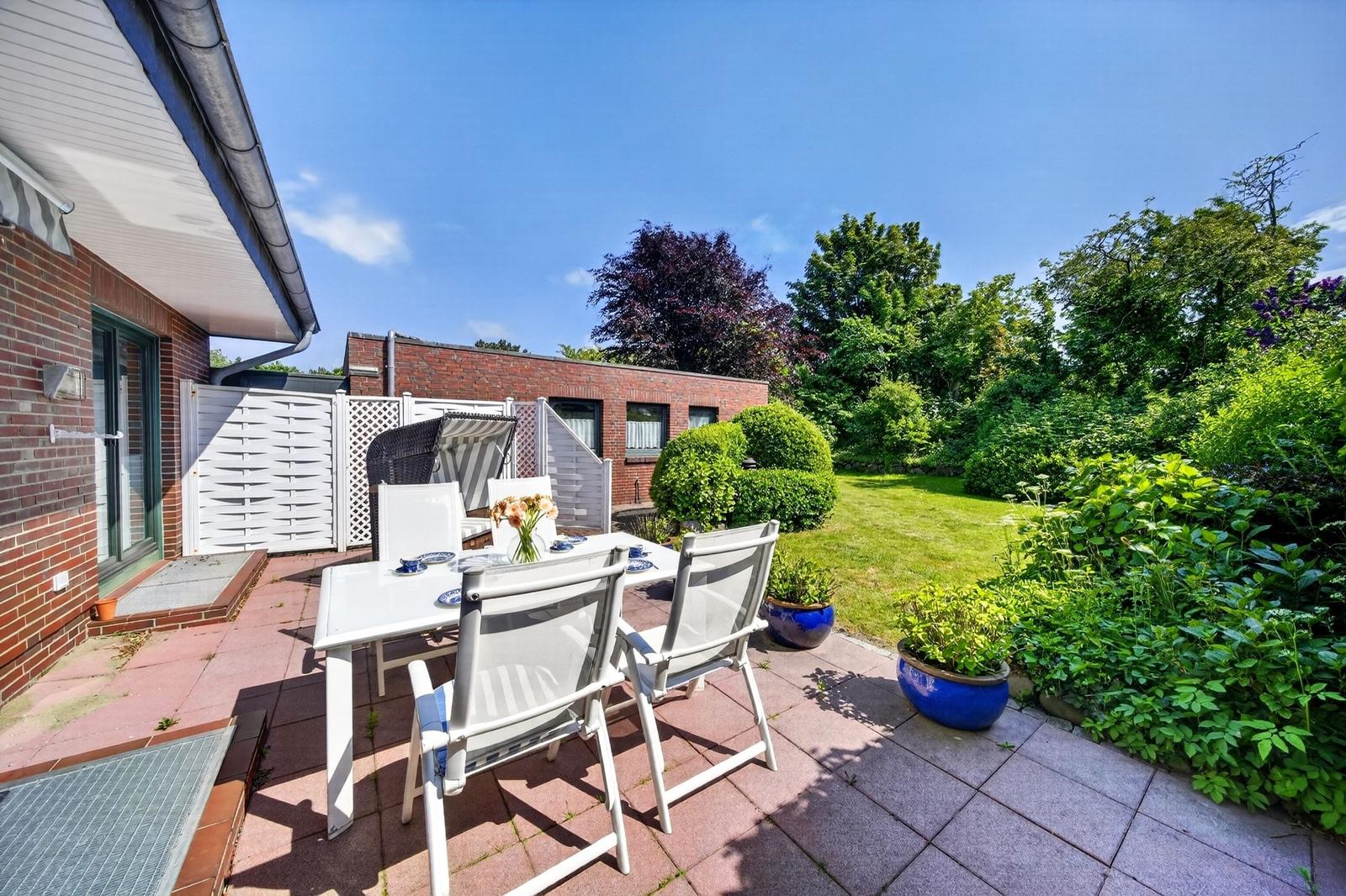 Terrasse mit Tisch, Stühlen und Pflanzen. Hinterhof mit Rasen und Bäumen.