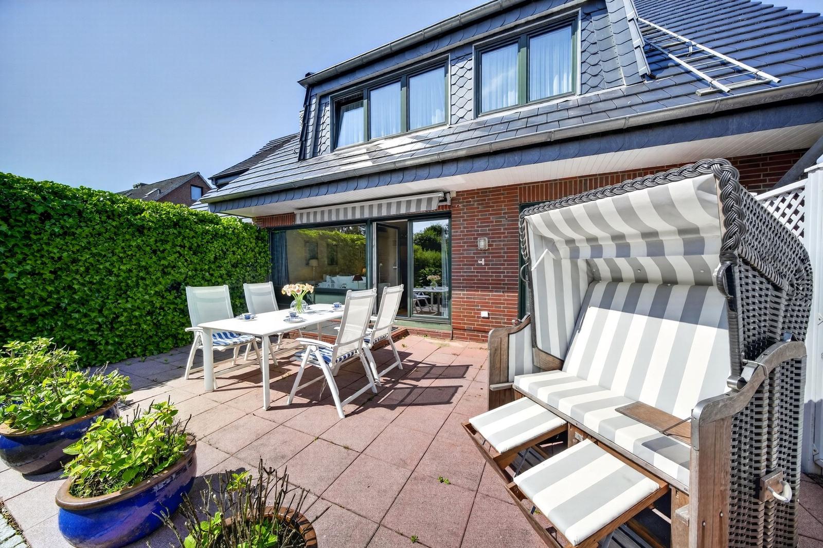 Terrasse mit Sitzgruppe, Strandkorb und Pflanzen vor einem Haus mit Dachfenstern.