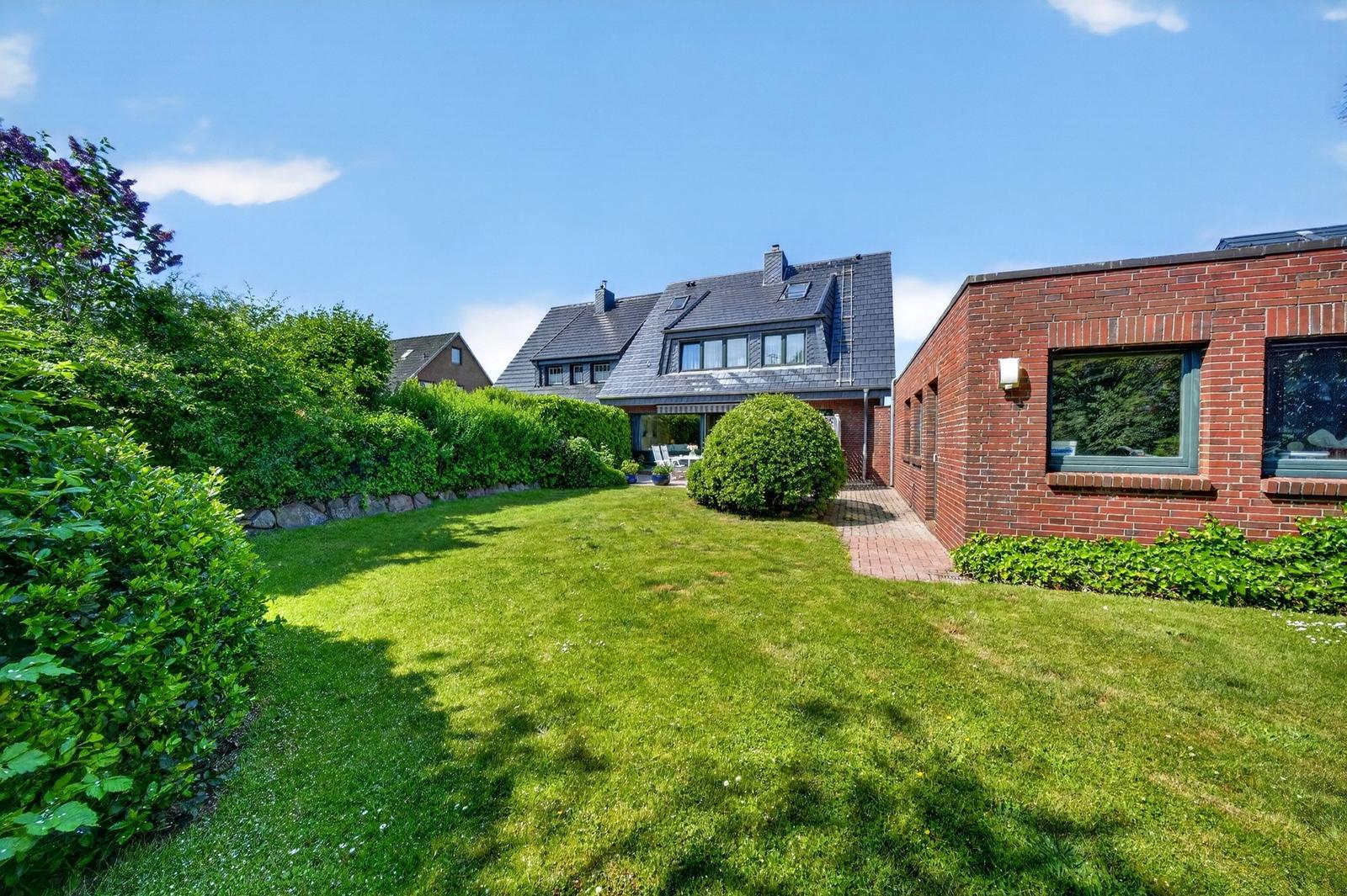 Haus mit Garten, Terrasse und rotem Backsteinbau. Grünflächen und Bäume umgeben die Immobilie.