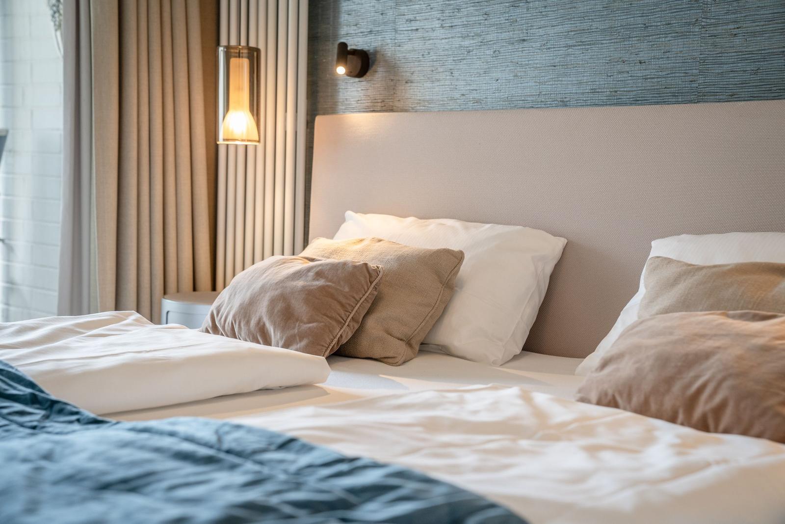 Ein Bett mit Kissen und Decke, Wandbeleuchtung und Vorhang im Hintergrund.